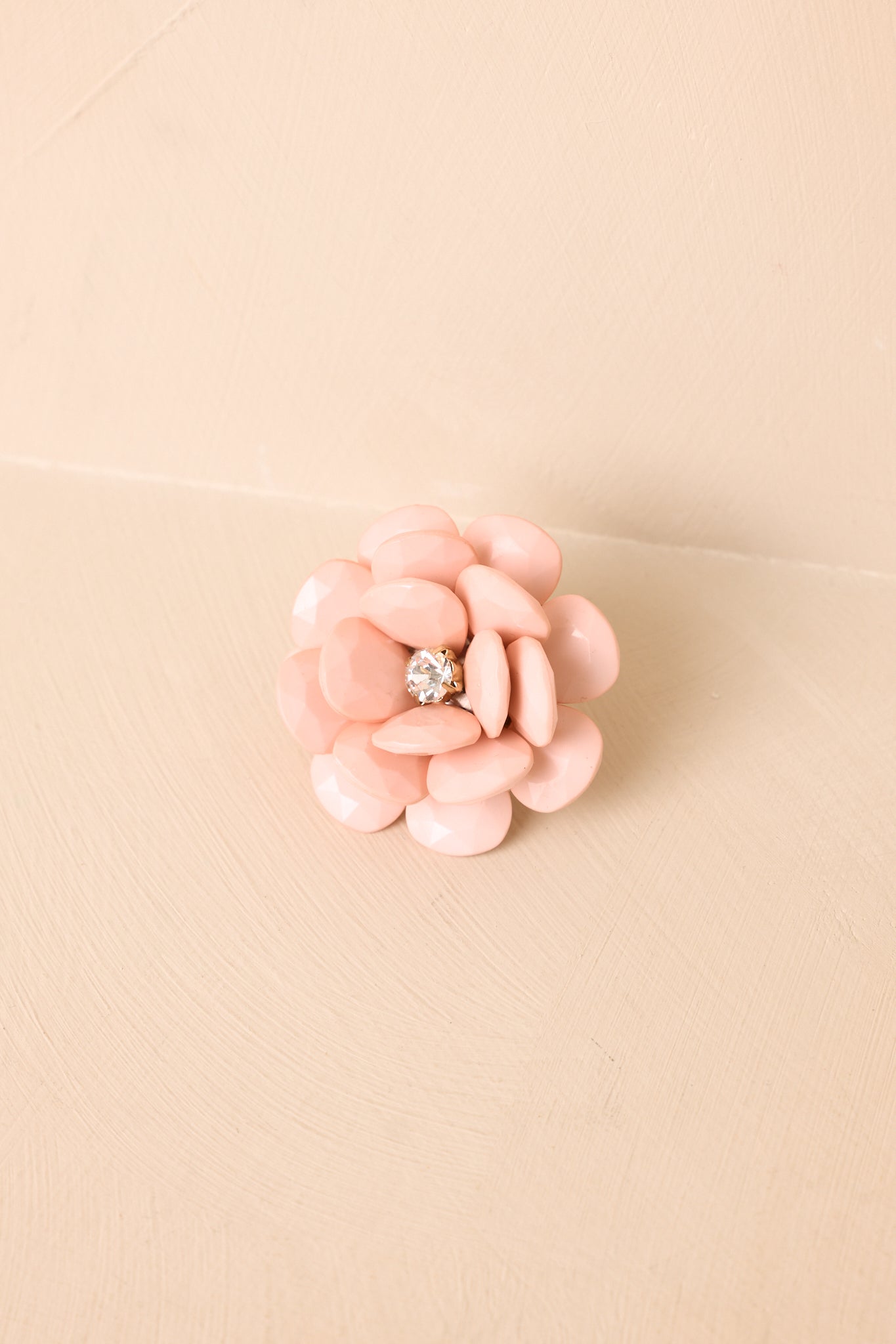 Angled view of pink oversized floral ring on a beige background emphasizing its dimensional, bloom-like design.
