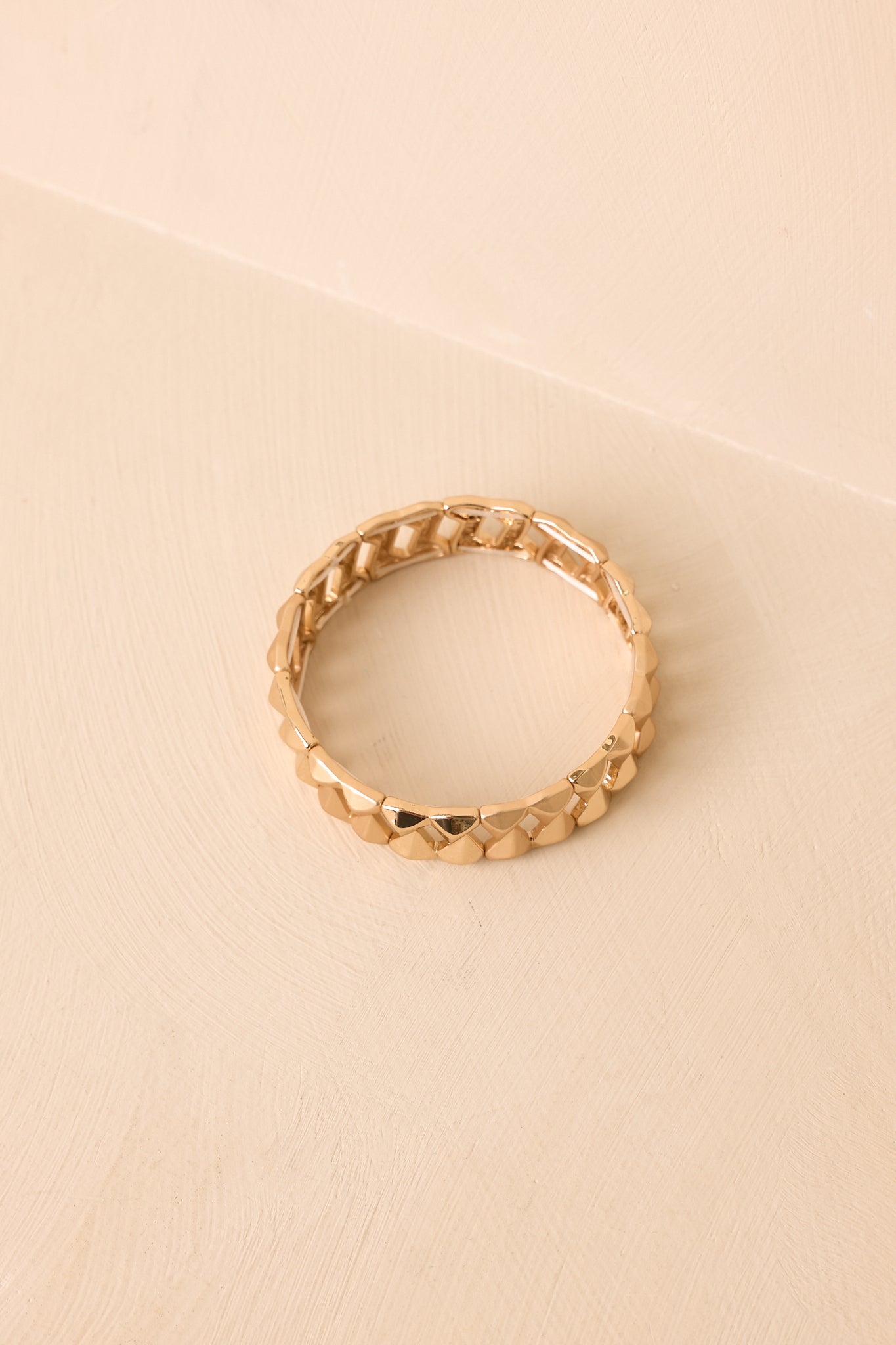 Angled view of gold stretch bracelet on a beige background emphasizing the structured link pattern and elastic fit.