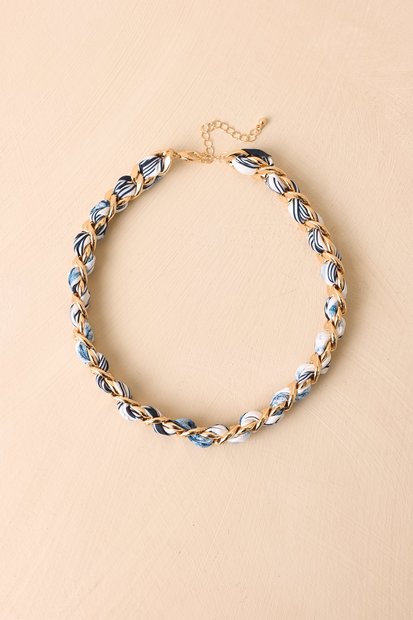Cropped view of gold-tone chain necklace woven with blue patterned scarf fabric in choker length.