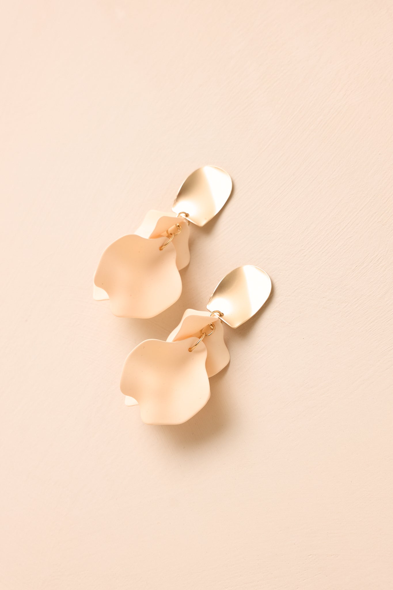 Angled view of gold stud floral earrings on beige backdrop highlighting soft color gradient and movement.