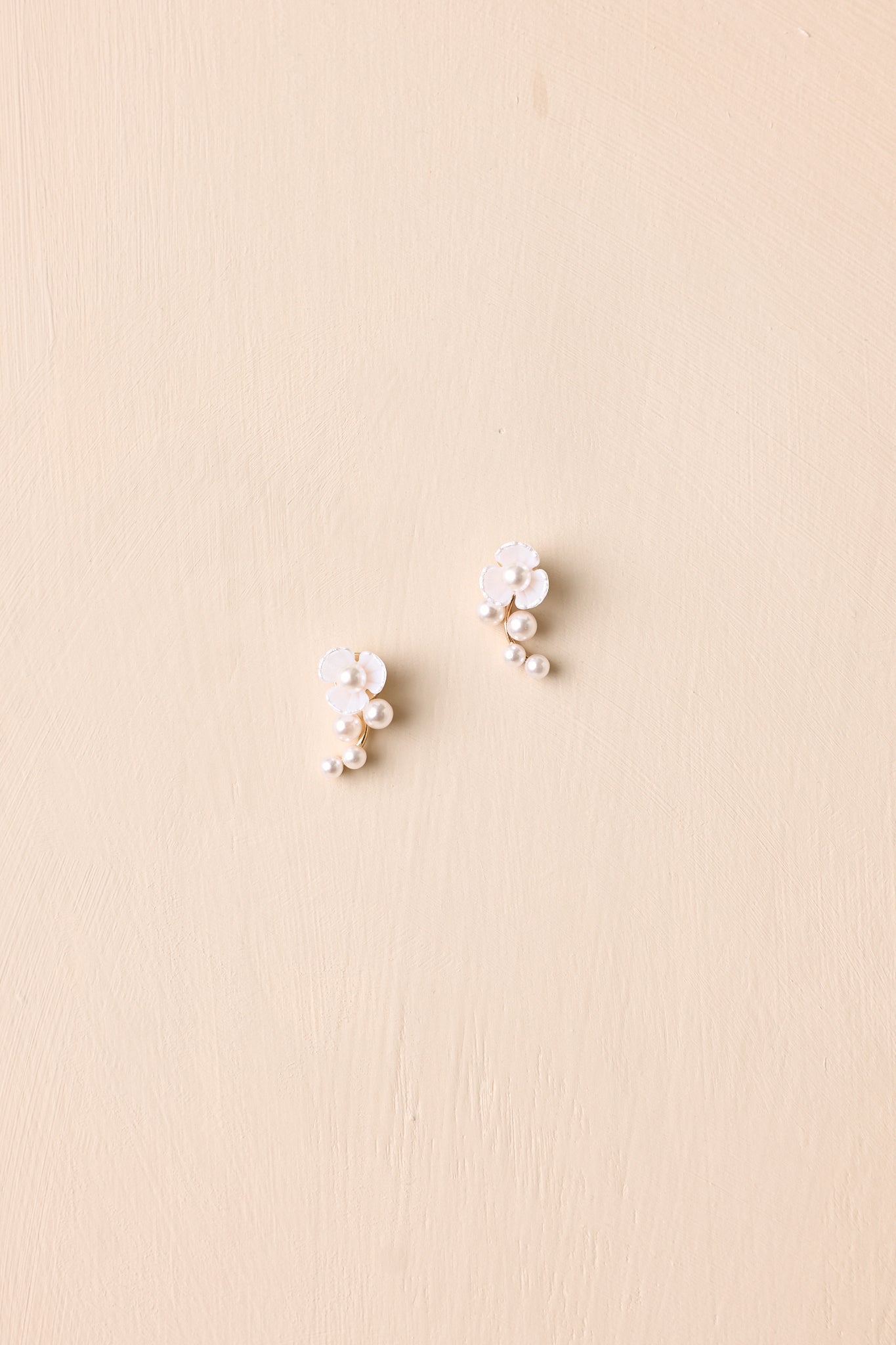 Front view of pearl flower drop earrings displayed on beige background emphasizing romantic floral shape.