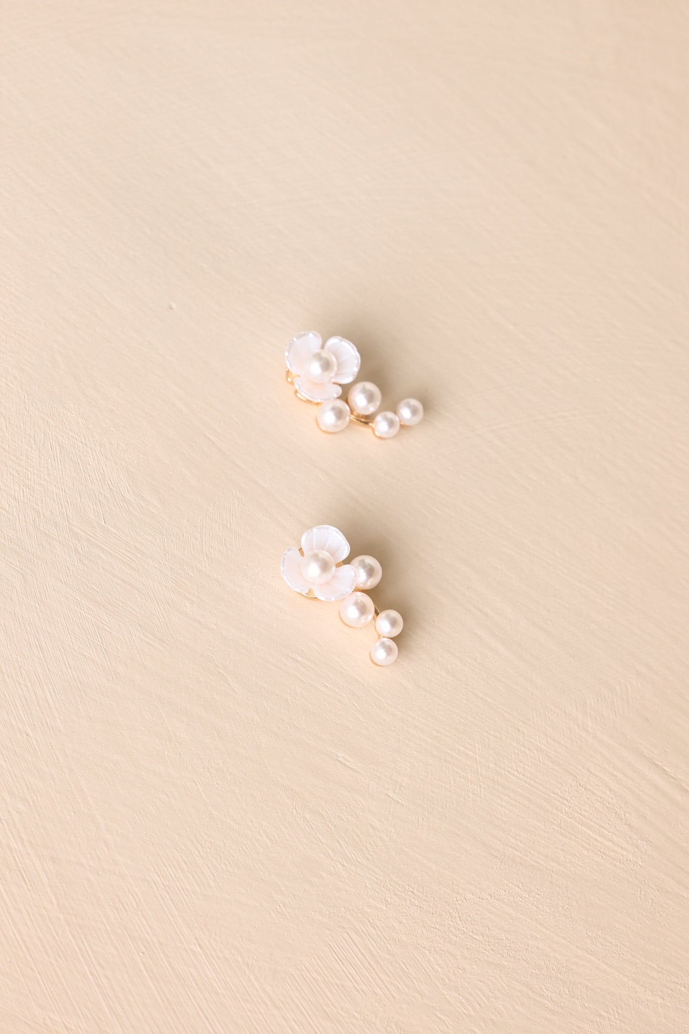 Angled view of gold floral earrings on beige backdrop highlighting pearl accents and delicate drop detail.