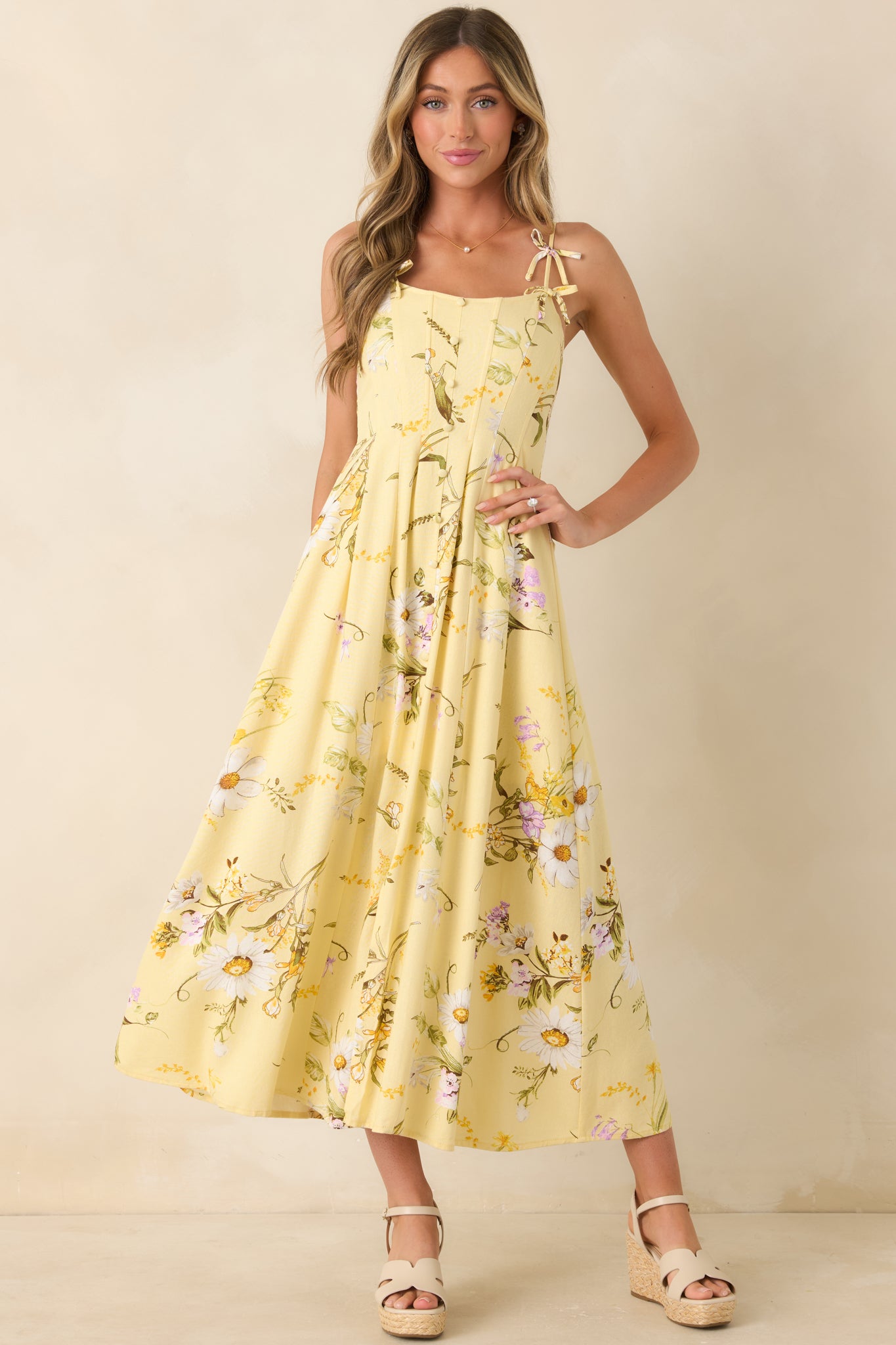 Warm yellow floral midi dress featuring a button-front bodice, adjustable straps with bow accents, and an airy draped silhouette.
