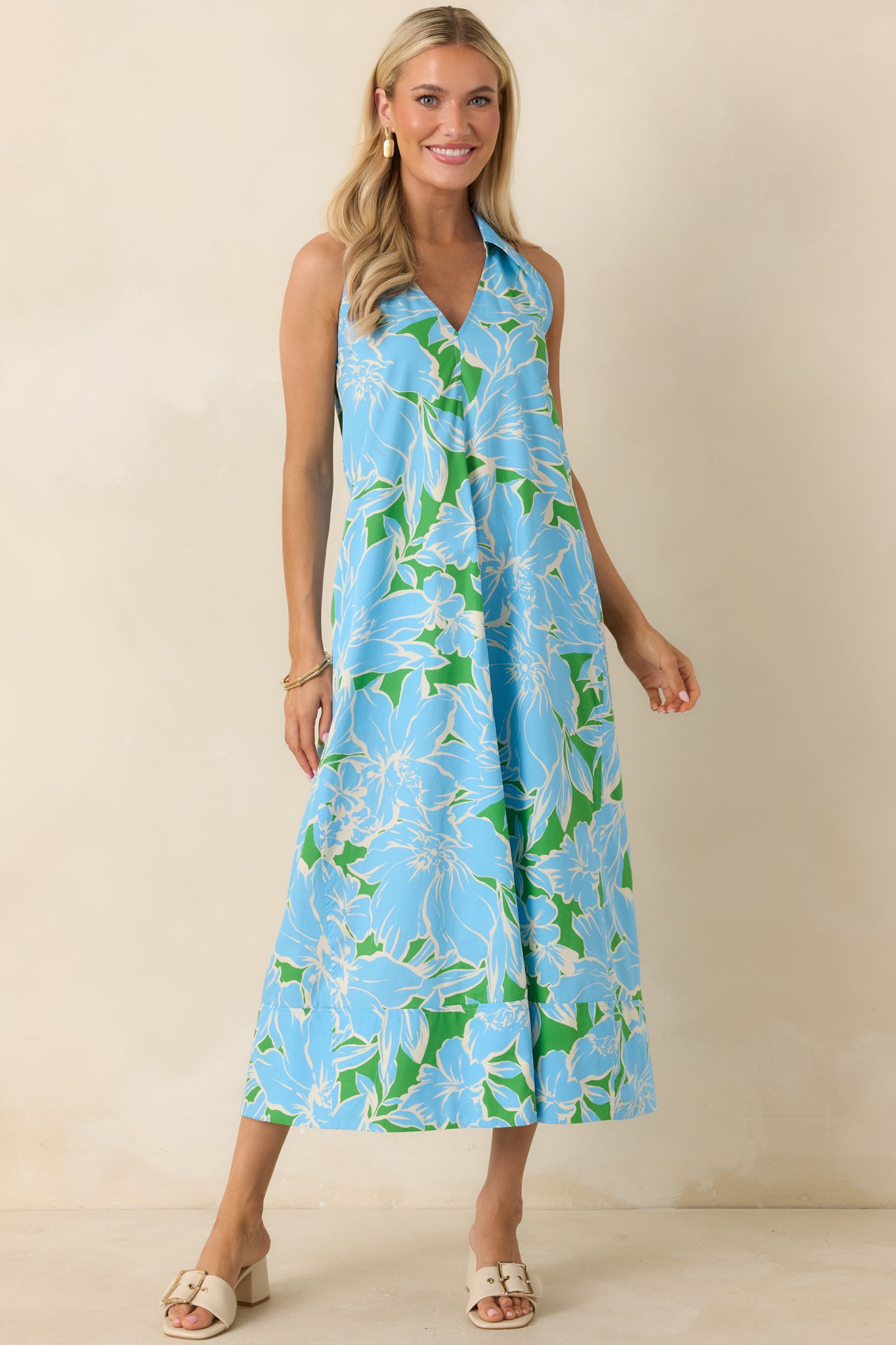 Light blue, green, and white floral midi dress featuring a collared V-neckline, sleeveless silhouette, side pockets, and a flowing cotton skirt.
