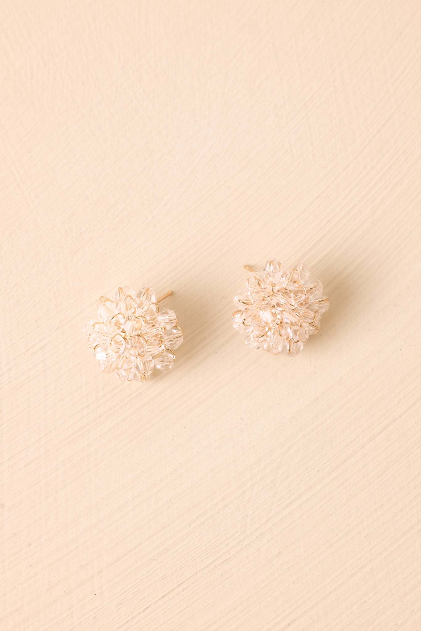 Pair of crystal floral stud earrings displayed on a beige background, featuring clustered clear beads and a refined floral shape.