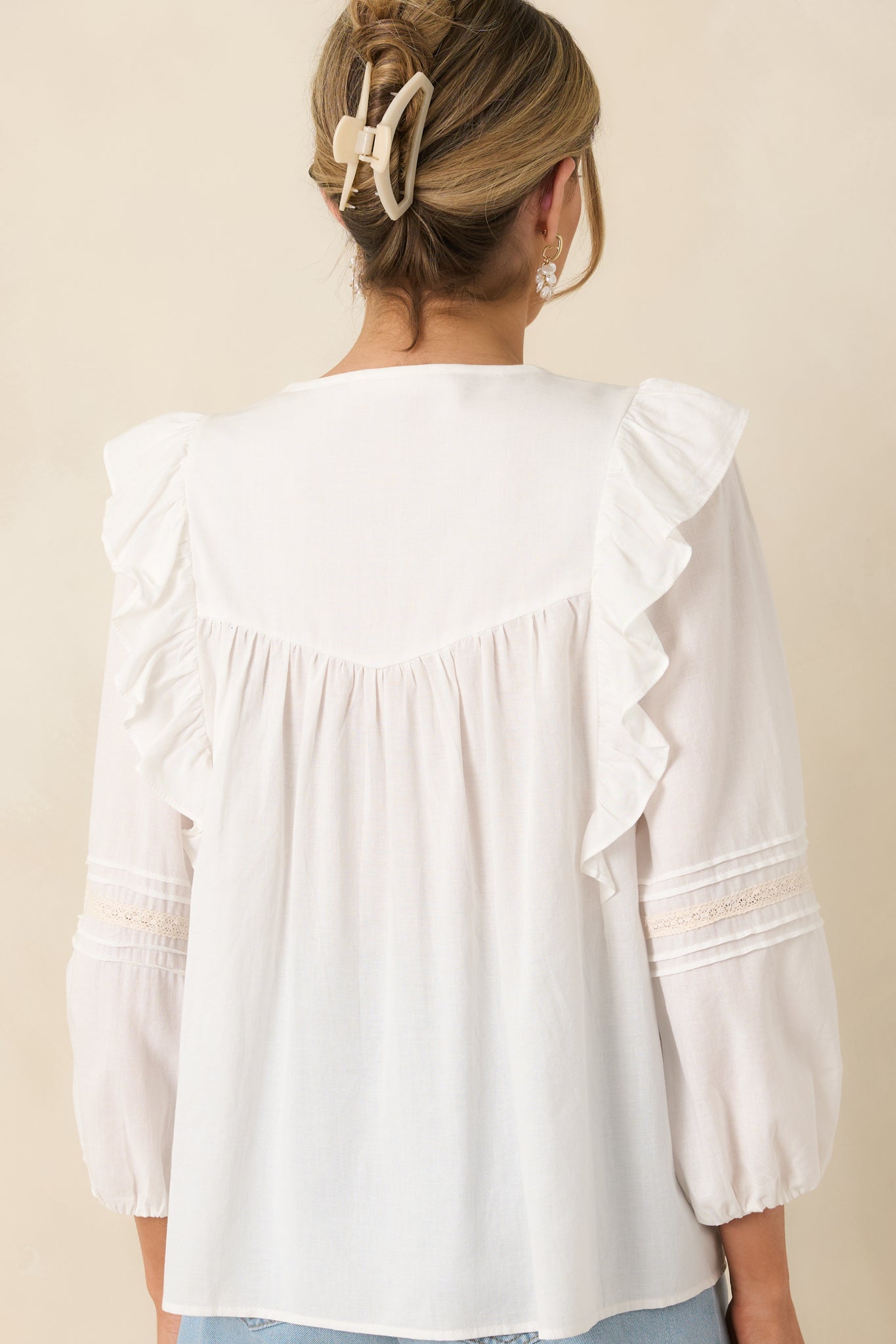 Rear view of white blouse with relaxed silhouette and sheer sleeves.