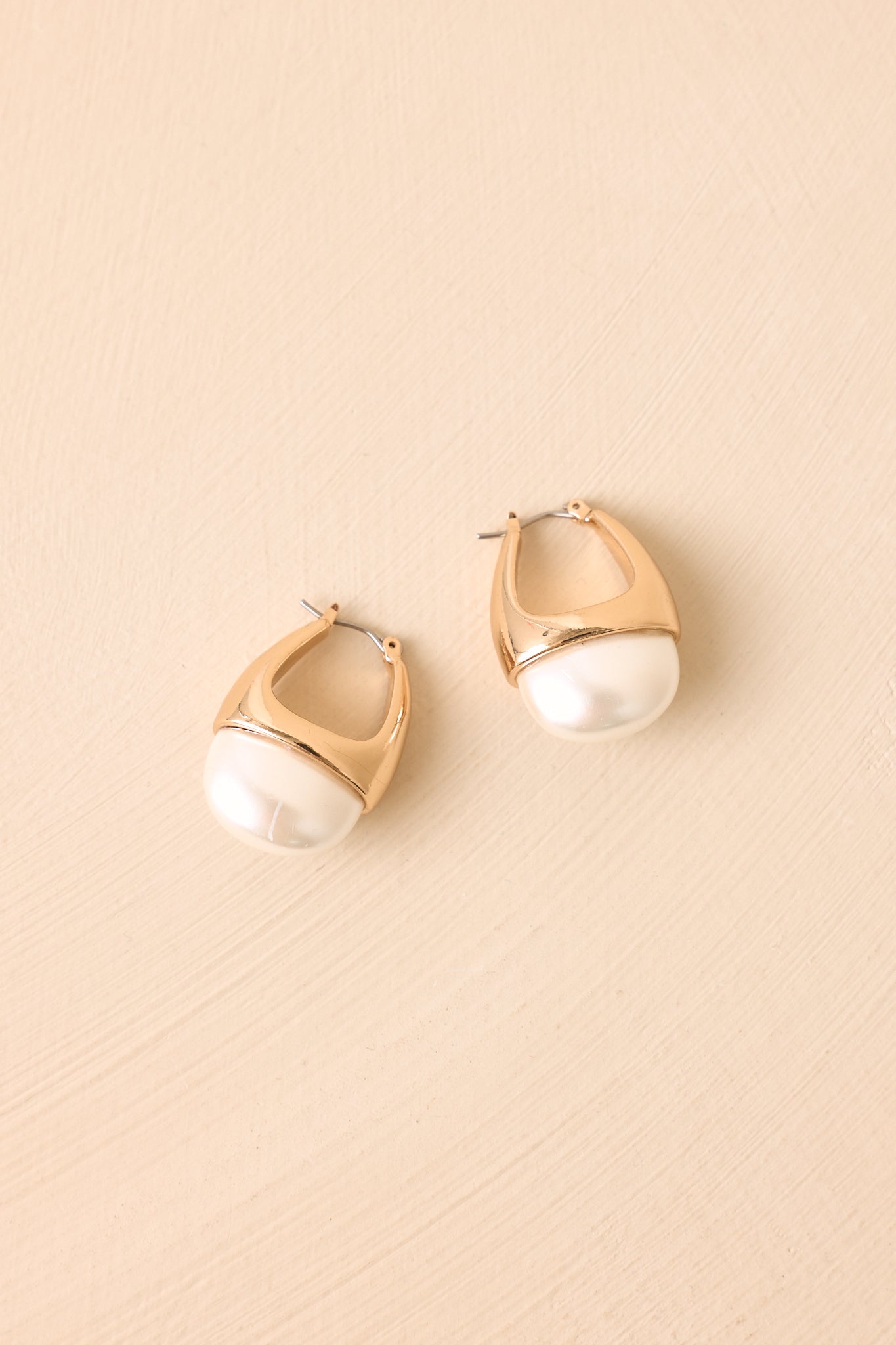 Pair of pearl hoop earrings displayed on a beige background, featuring oversized pearl accents and a sculpted gold-tone design.