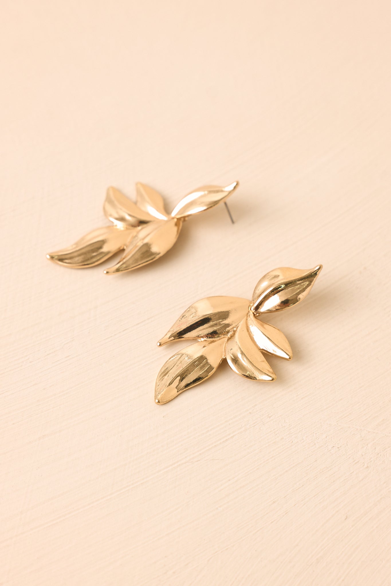 Gold leaf drop earrings displayed against a beige background, emphasizing the luminous finish and intricate layered design.