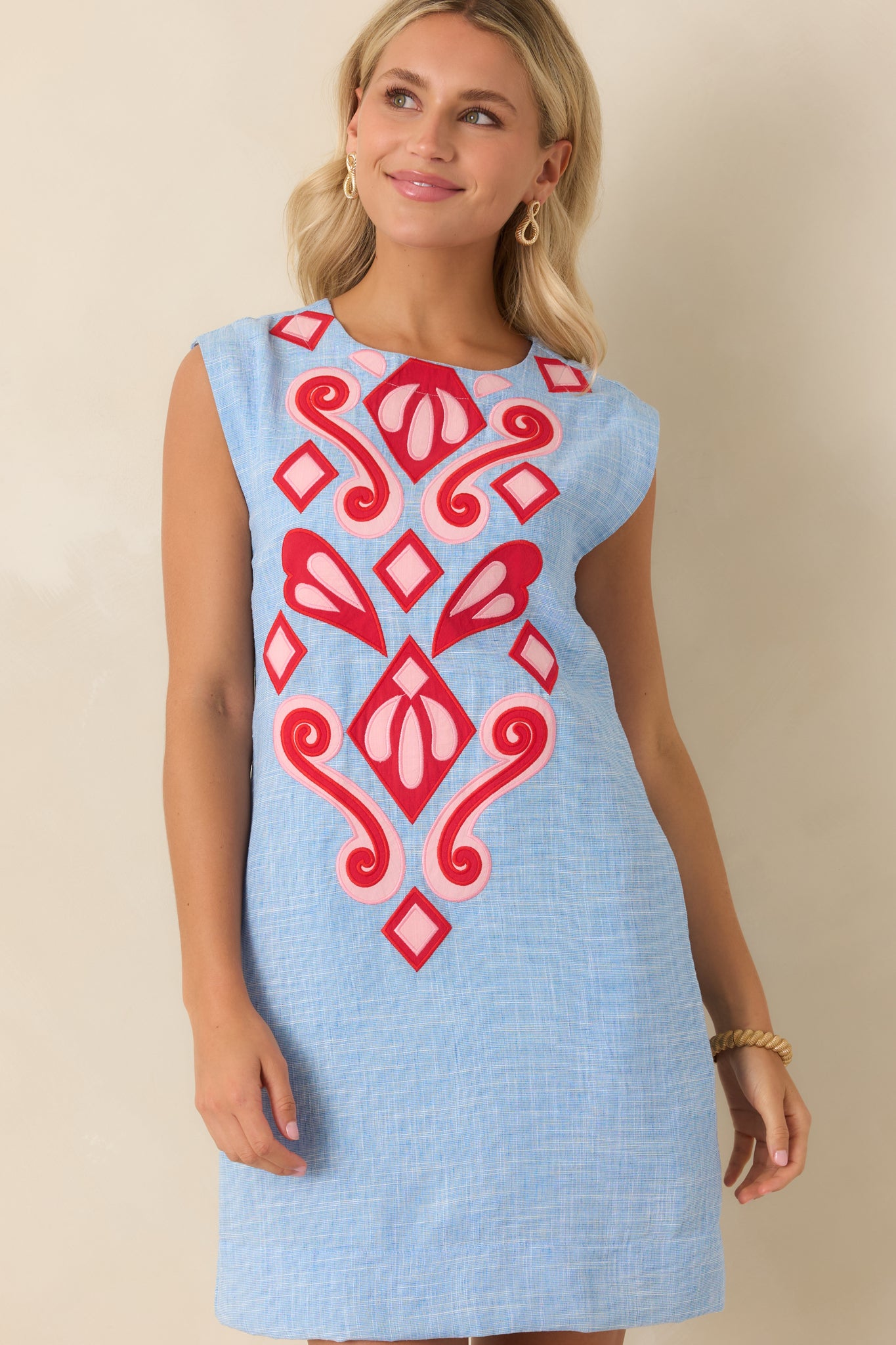 Blue sleeveless mini dress with straight silhouette and intricate appliqué detailing across the front panel.