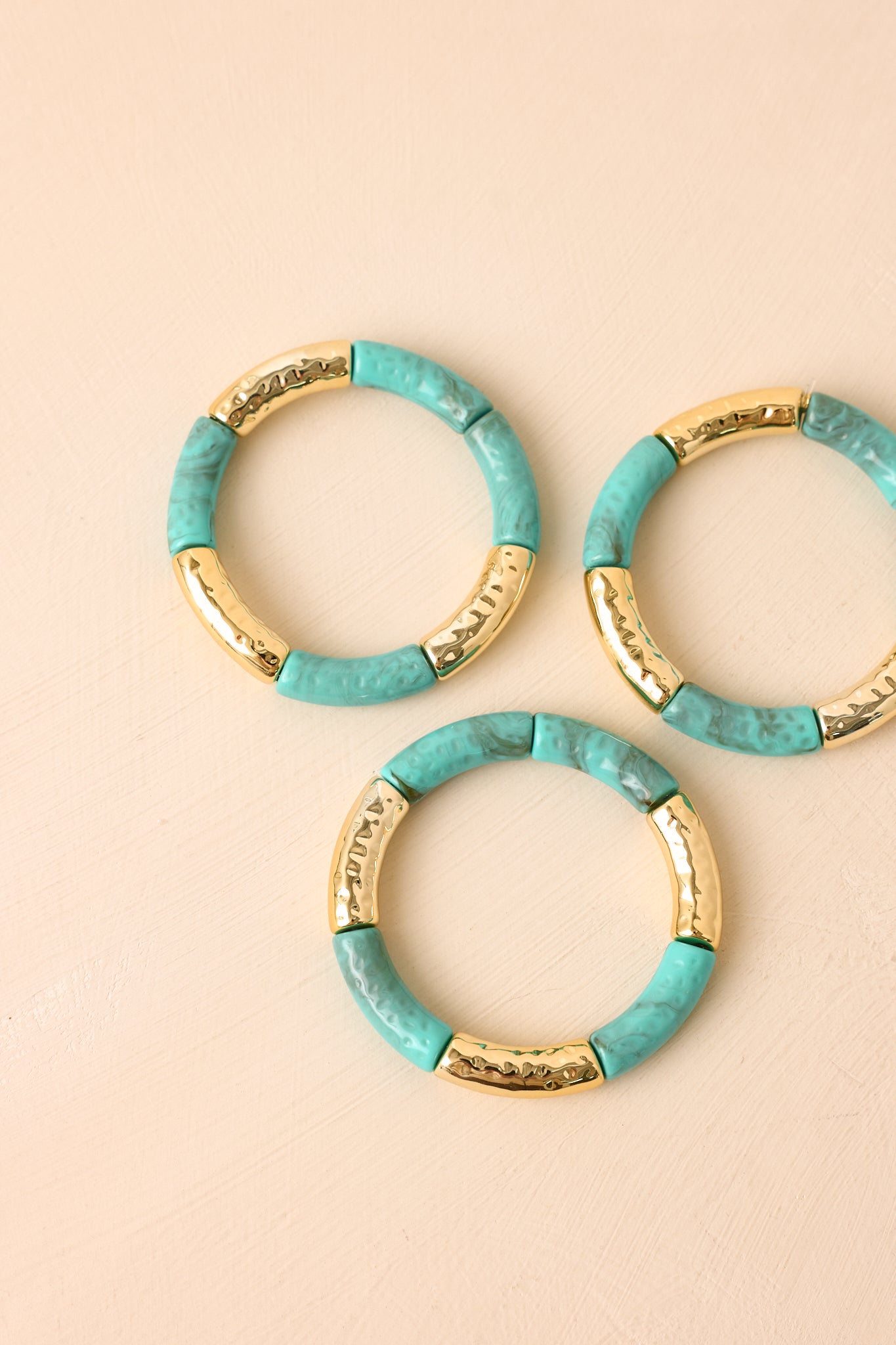 Turquoise and gold bracelet set displayed on a beige background, featuring rounded beads and polished metallic elements.