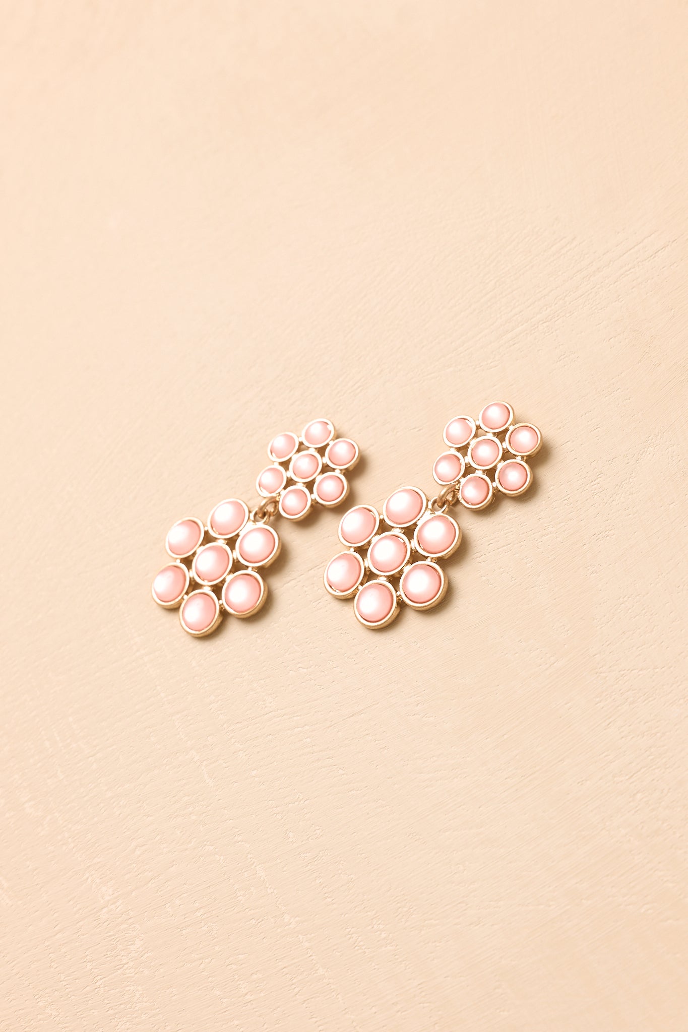 Pair of pink floral earrings displayed on a beige background, featuring layered petals and elegant gold-tone edging.