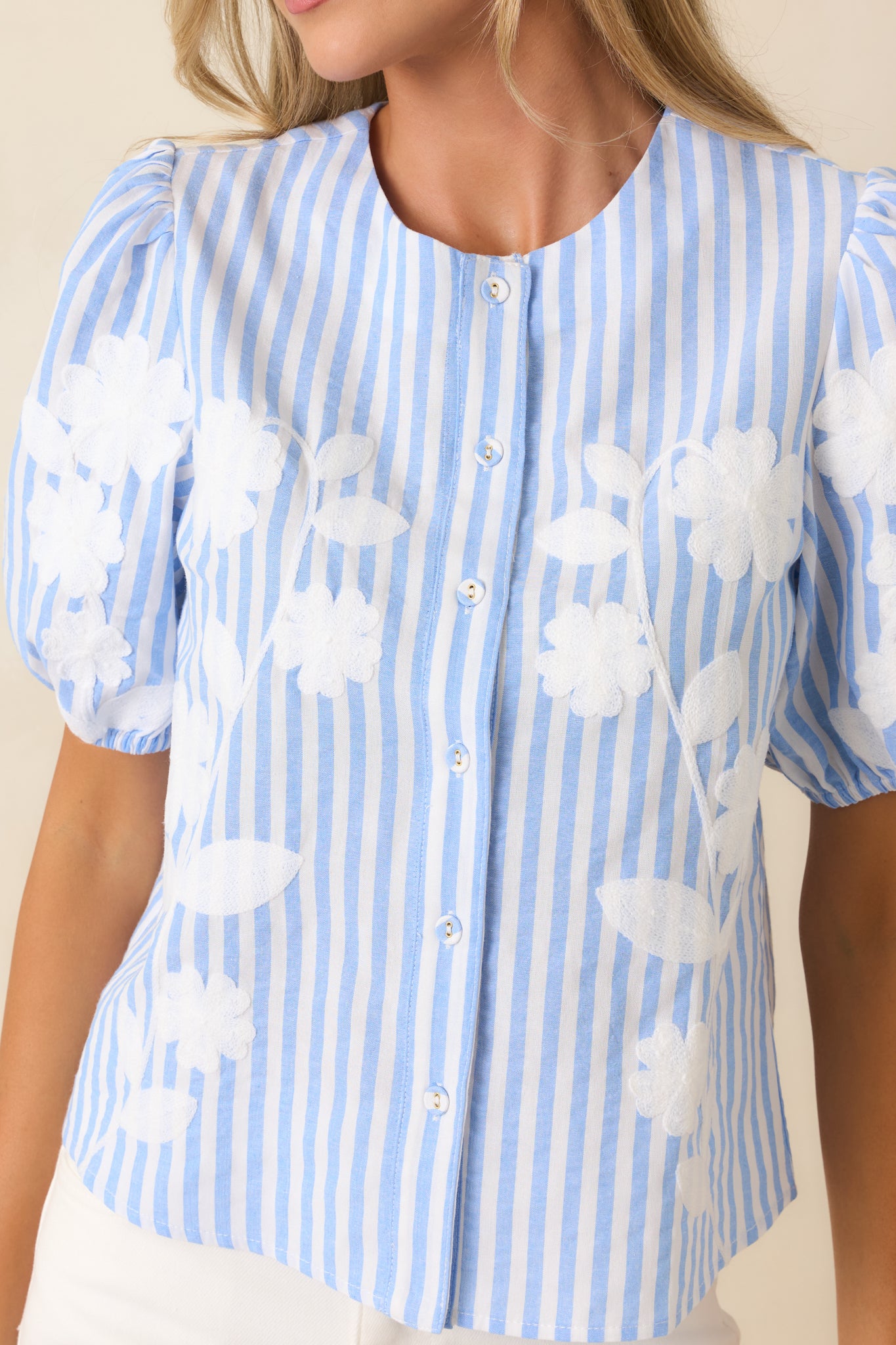 Detailed view of puff sleeve gathering and button-front construction on collarless top.