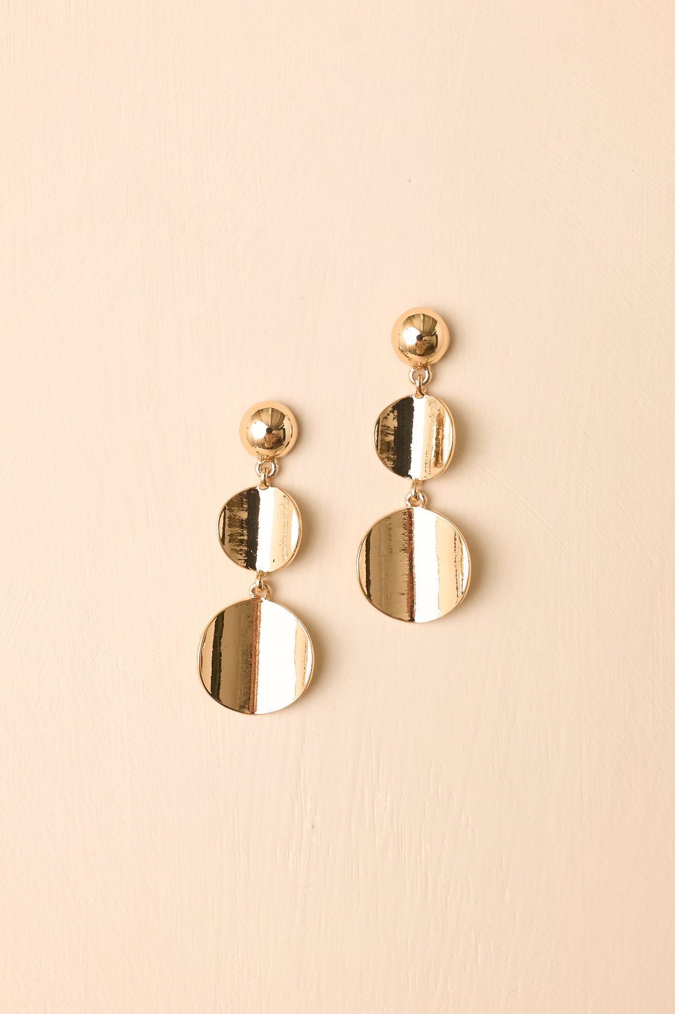 Pair of gold drop earrings displayed on a beige background, featuring graduated discs and a luminous high-shine finish.