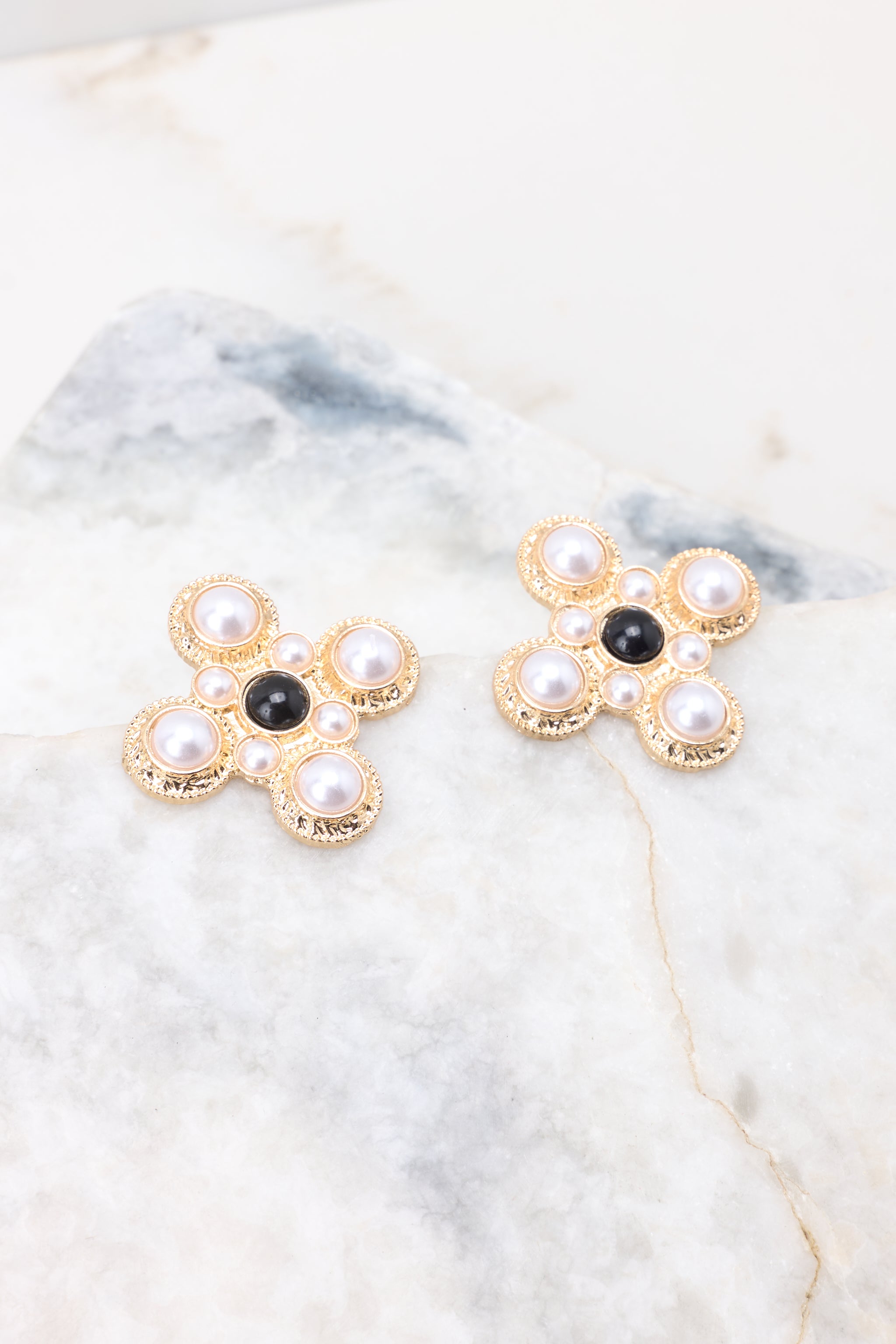 Angled view of these earrings that feature a fun abstract shape, gold hardware, and white and black pearl detailing.