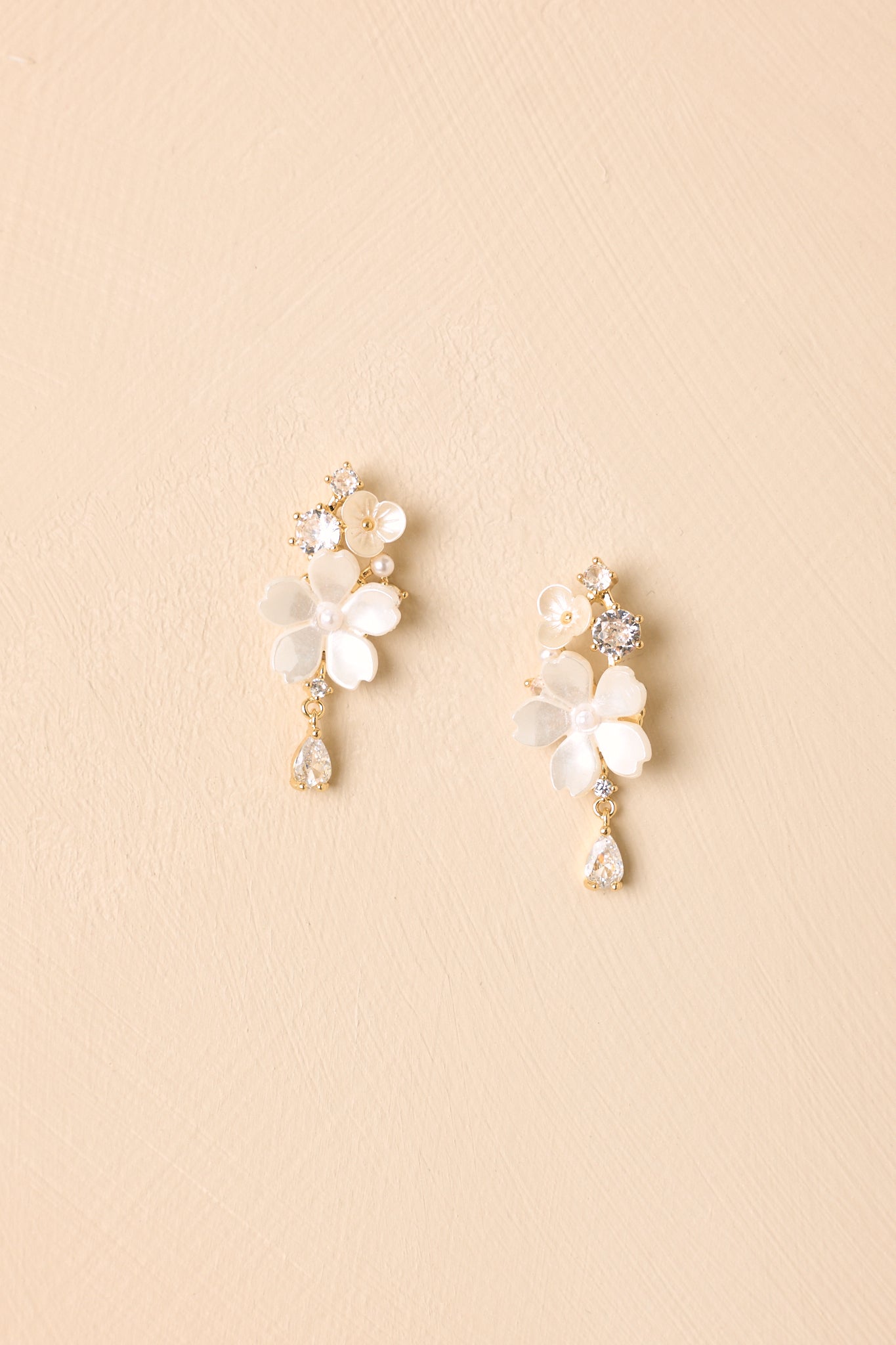 Pair of pearlescent floral drop earrings displayed on a beige background, featuring gold-tone details and crystal accents.
