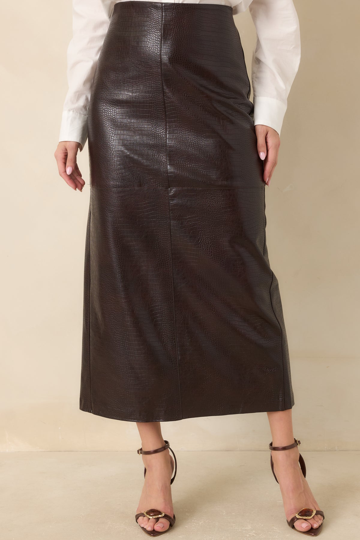 Defined panel seams run through the crocodile-textured brown faux leather skirt, creating a structured, streamlined appearance.