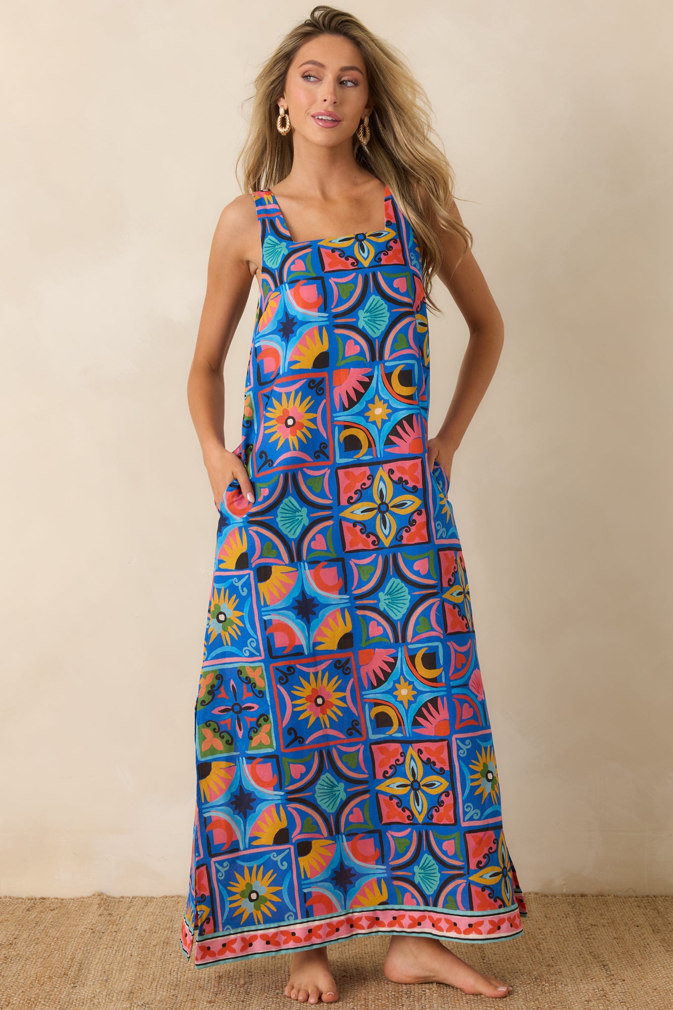 Mediterranean-inspired maxi dress featuring a vibrant blue pattern, wide straps, side pockets, and an airy flowing shape.
