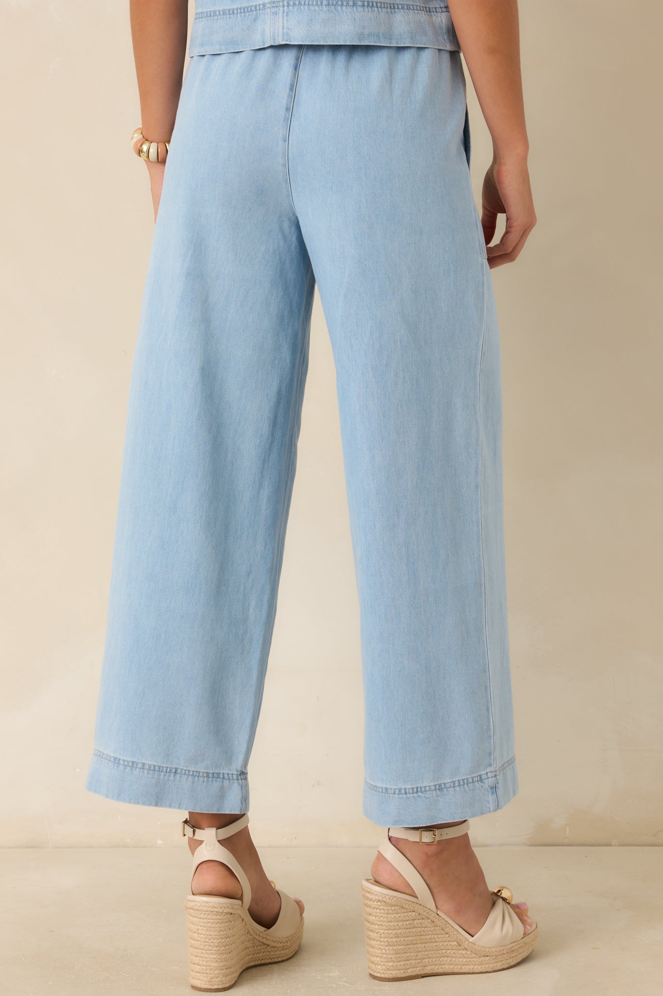 Rear view of light wash denim wide leg pants with elastic waistband and relaxed fit.