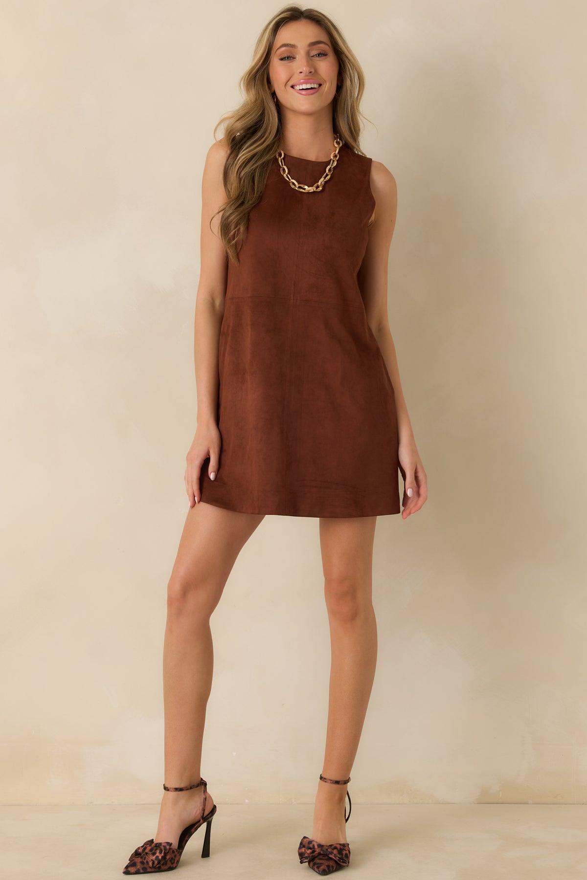 The cognac-brown faux suede mini dress features a rounded neckline, clean sleeveless design, and softly structured A-line shape.