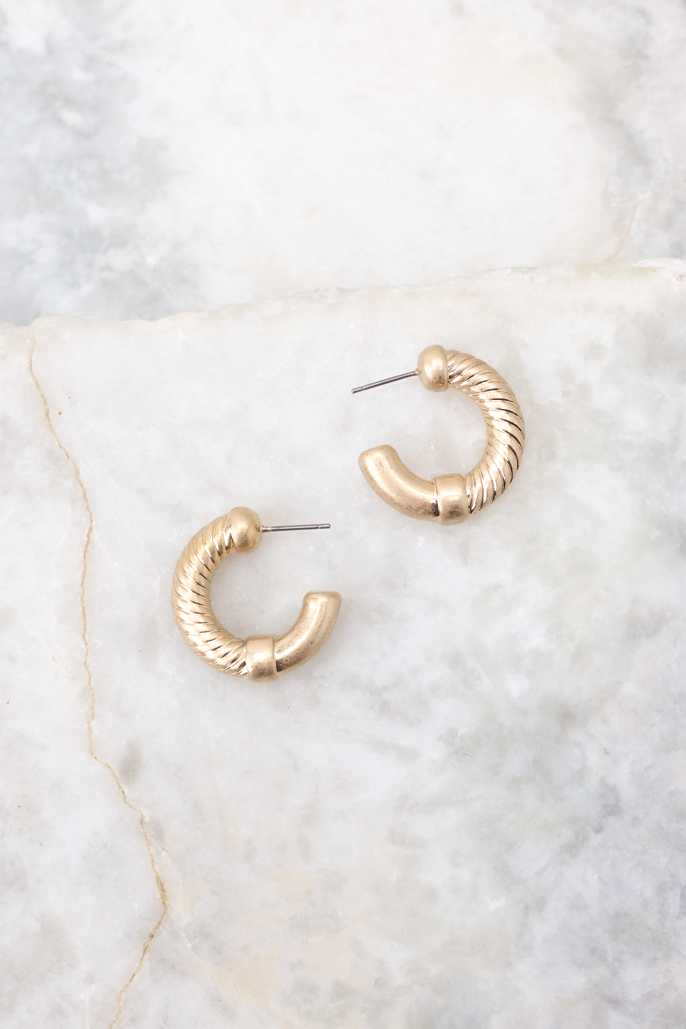 Close up view of these earrings that feature a textured design, worn gold finish, and secure post-back fastenings.