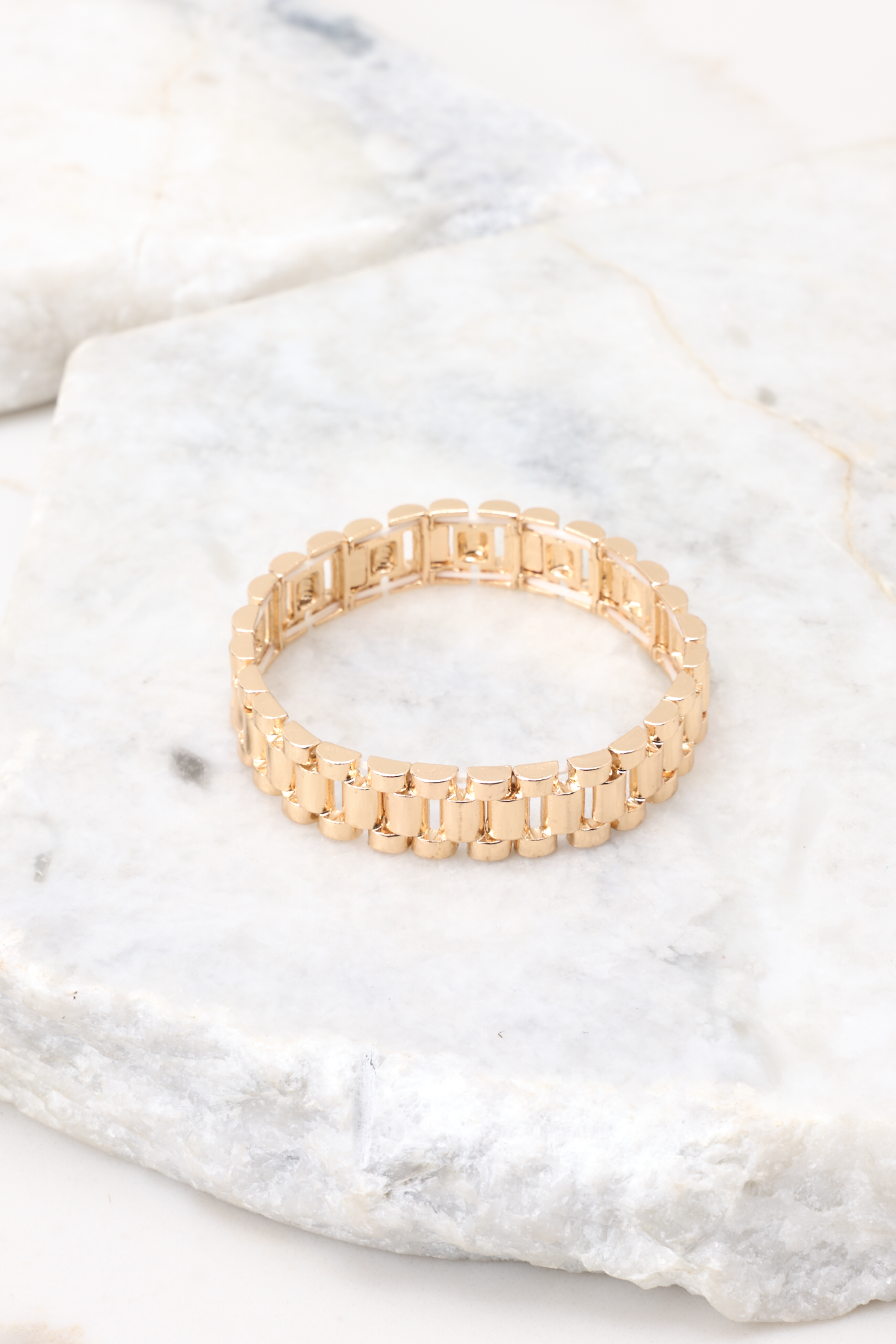 Overhead view of bracelet that features gold hardware, watch stretch band, and a slip-on style.