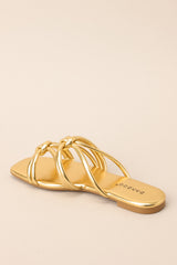 Inner-side view of these gold sandals that feature gold knotted straps, and a slip on design.