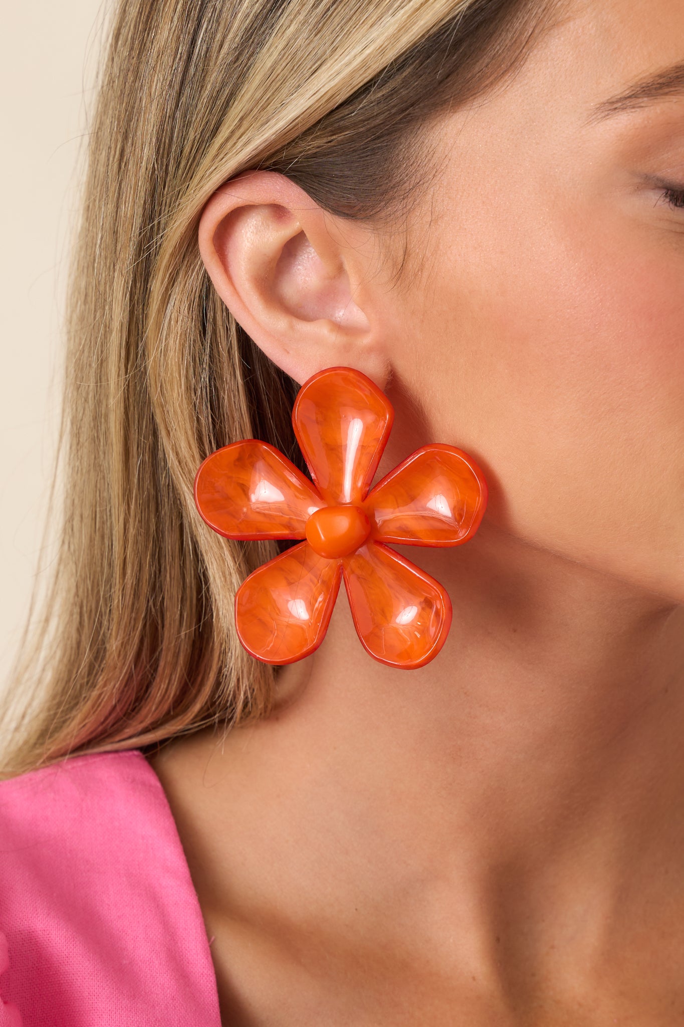 Close-up of orange floral drop earrings highlighting the layered oversized petals and vibrant high-gloss surface.
