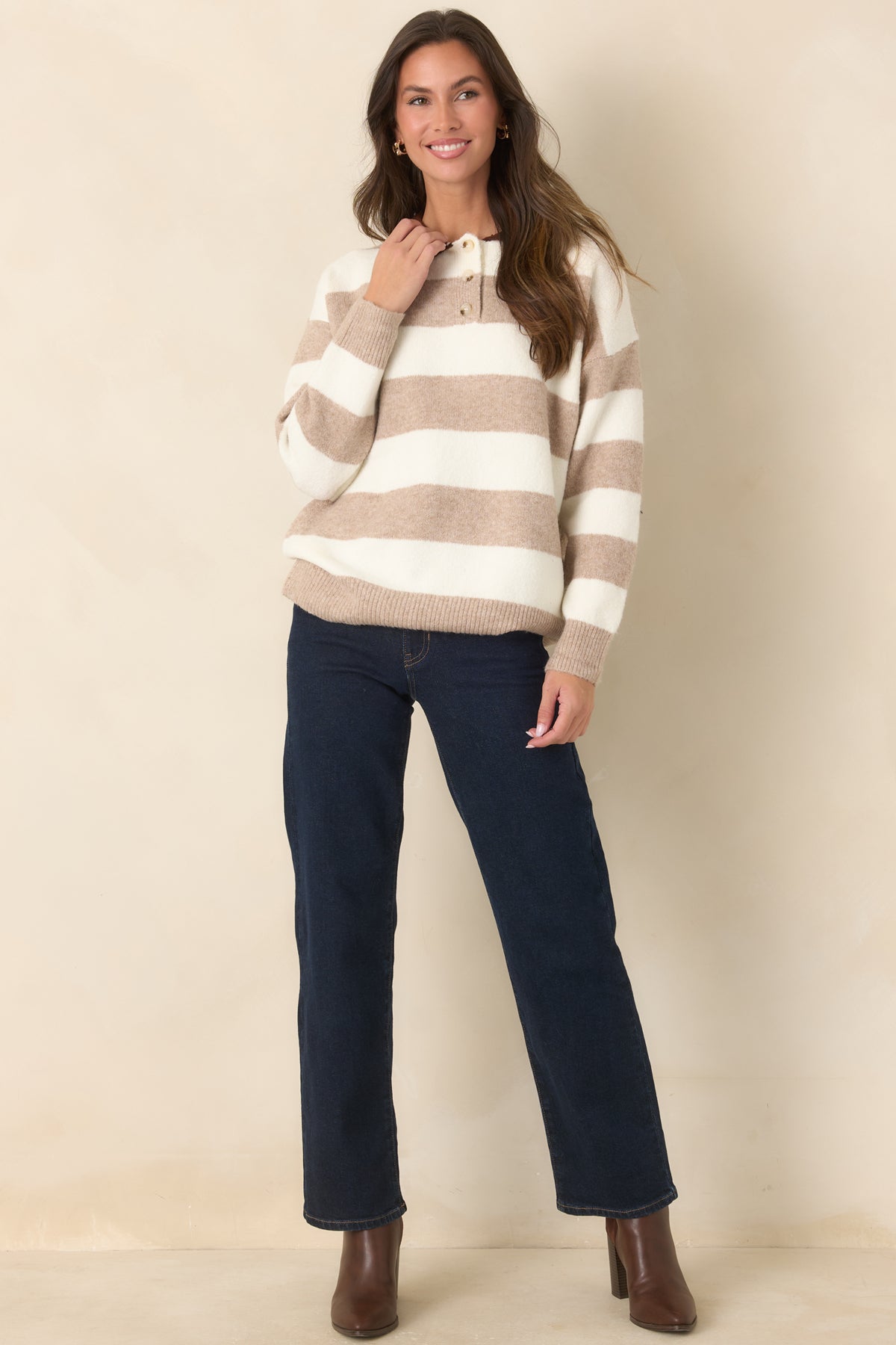 The cozy striped sweater features dropped shoulders, long sleeves, and a ribbed hem in a neutral ivory and brown palette.
