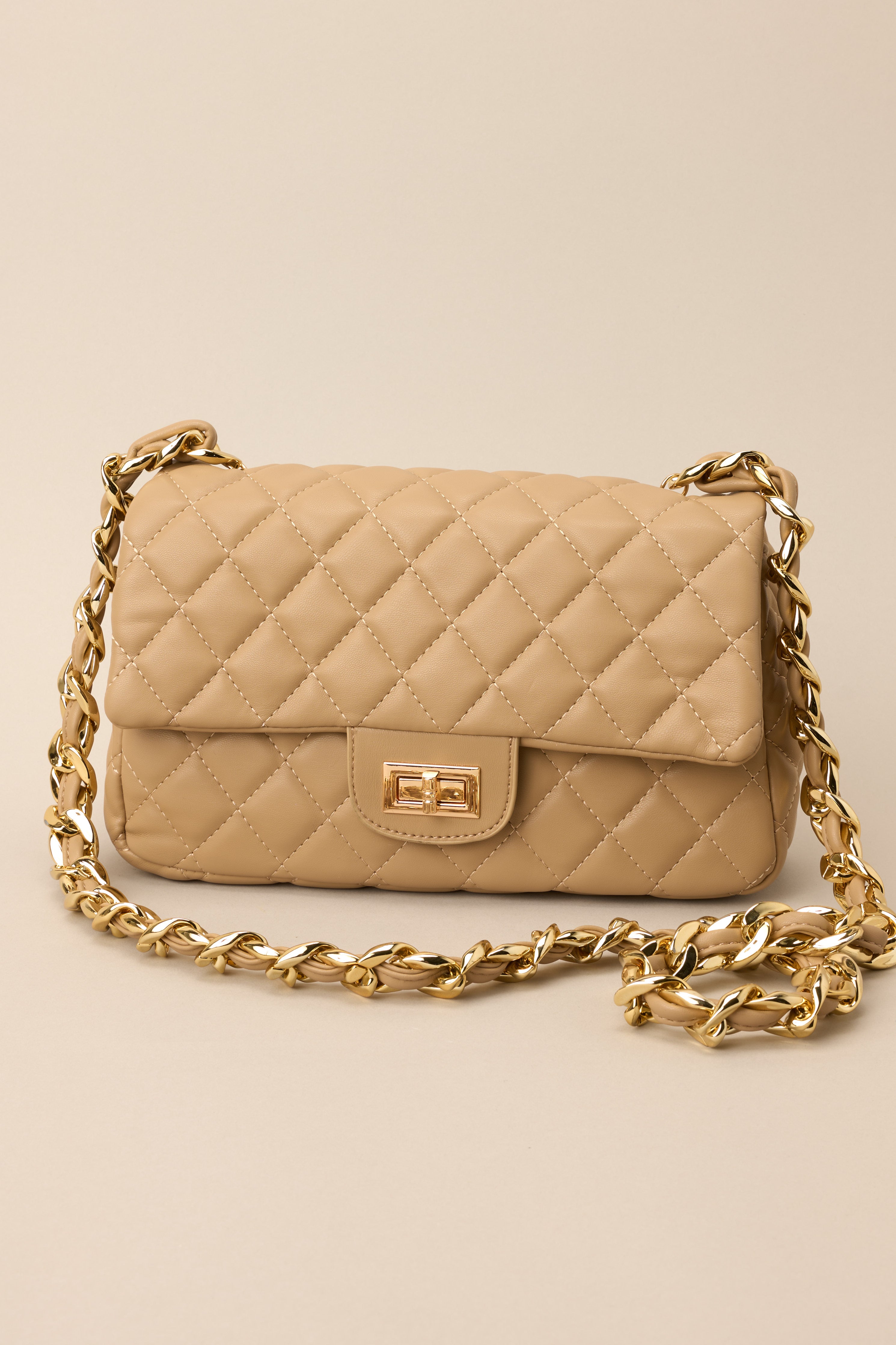Compact tan bag featuring quilted exterior, chain shoulder strap, and polished gold accents