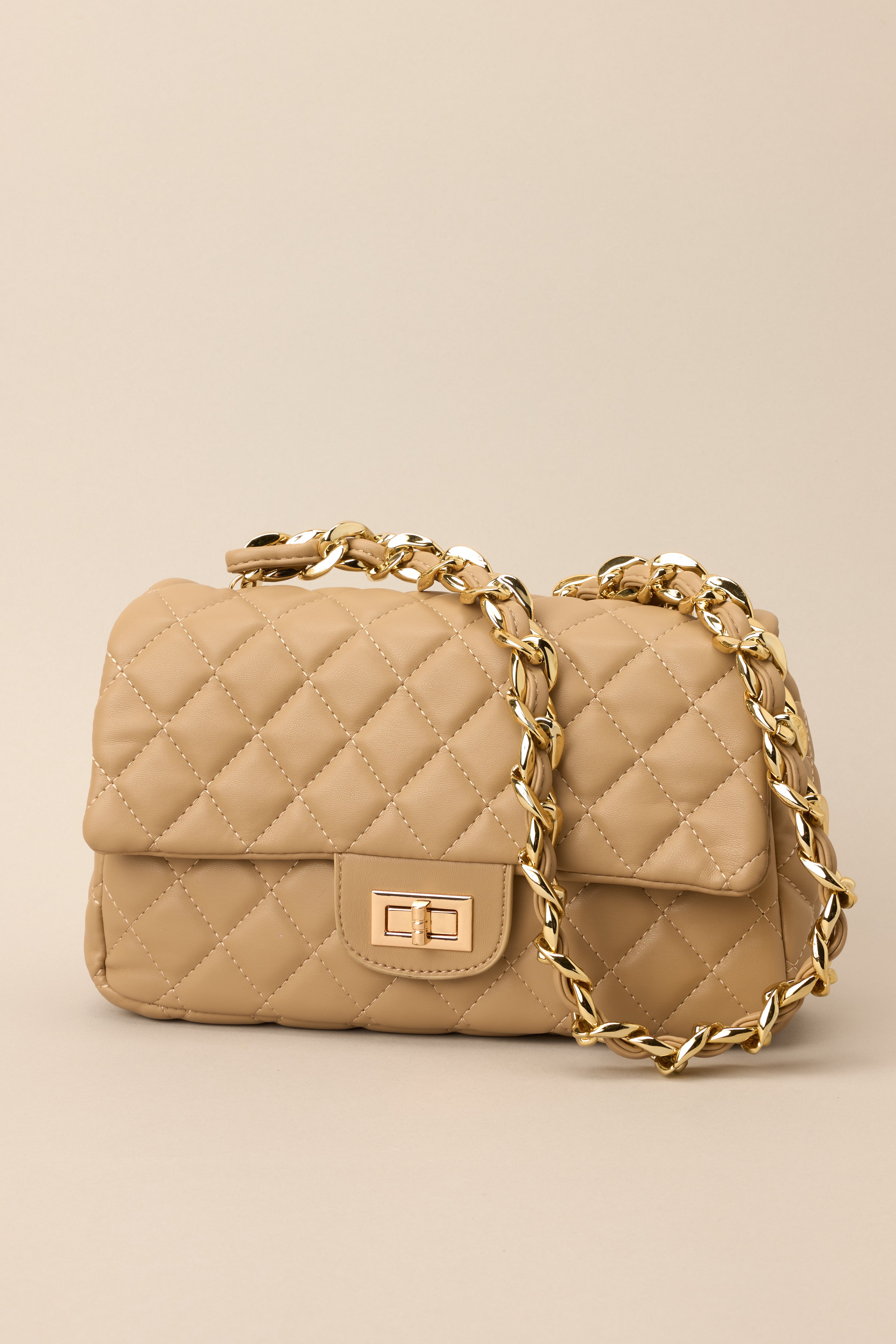Cropped view of tan handbag highlighting turn-lock closure and quilted texture