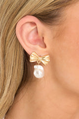 These earrings feature gold hardware, a delicate bow design, a faux freshwater pearl, and secure post backings.