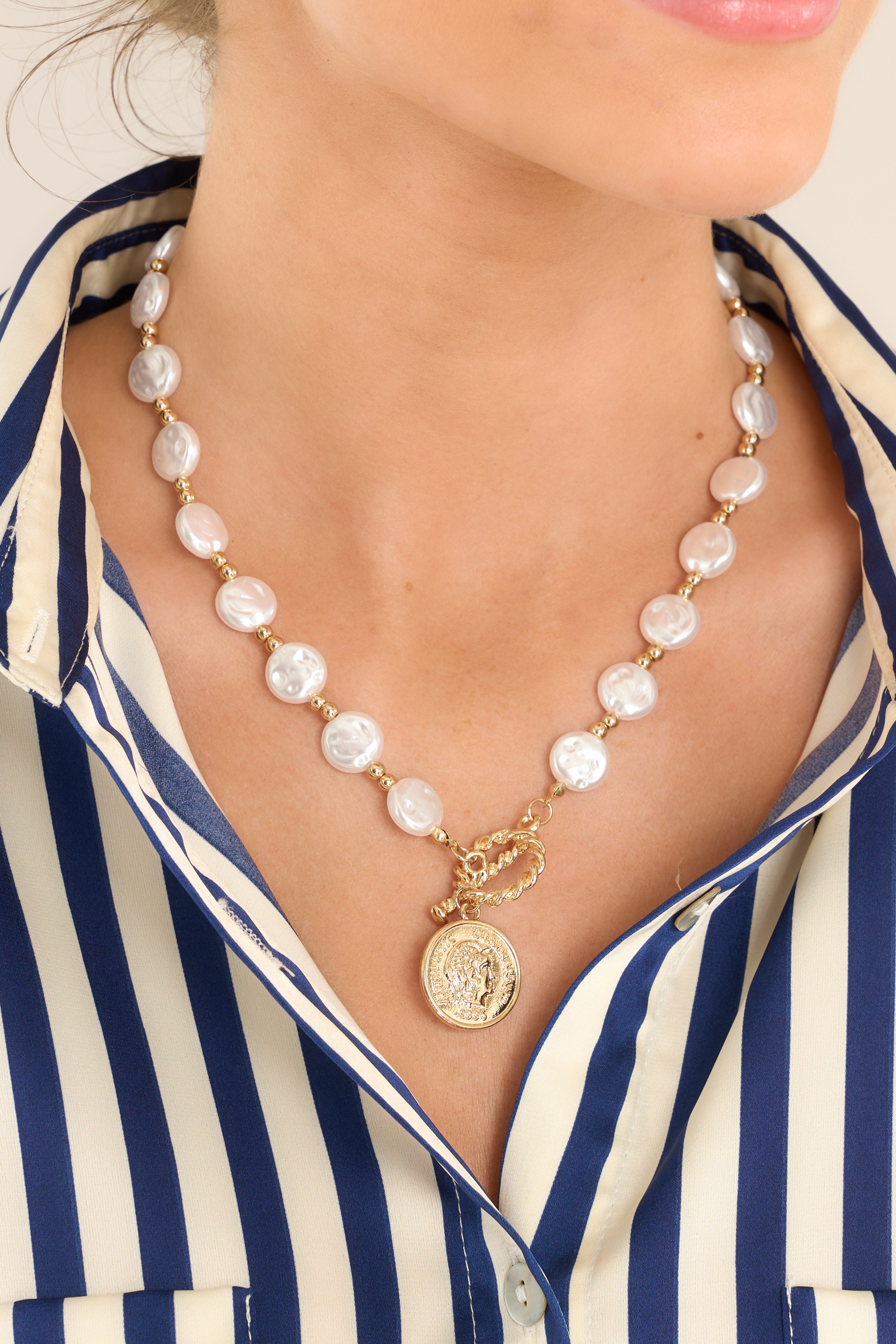 This gold and pearl necklace features gold hardware, flat faux pearls and small gold beads, a toggle closure, and a faux coin pendant.