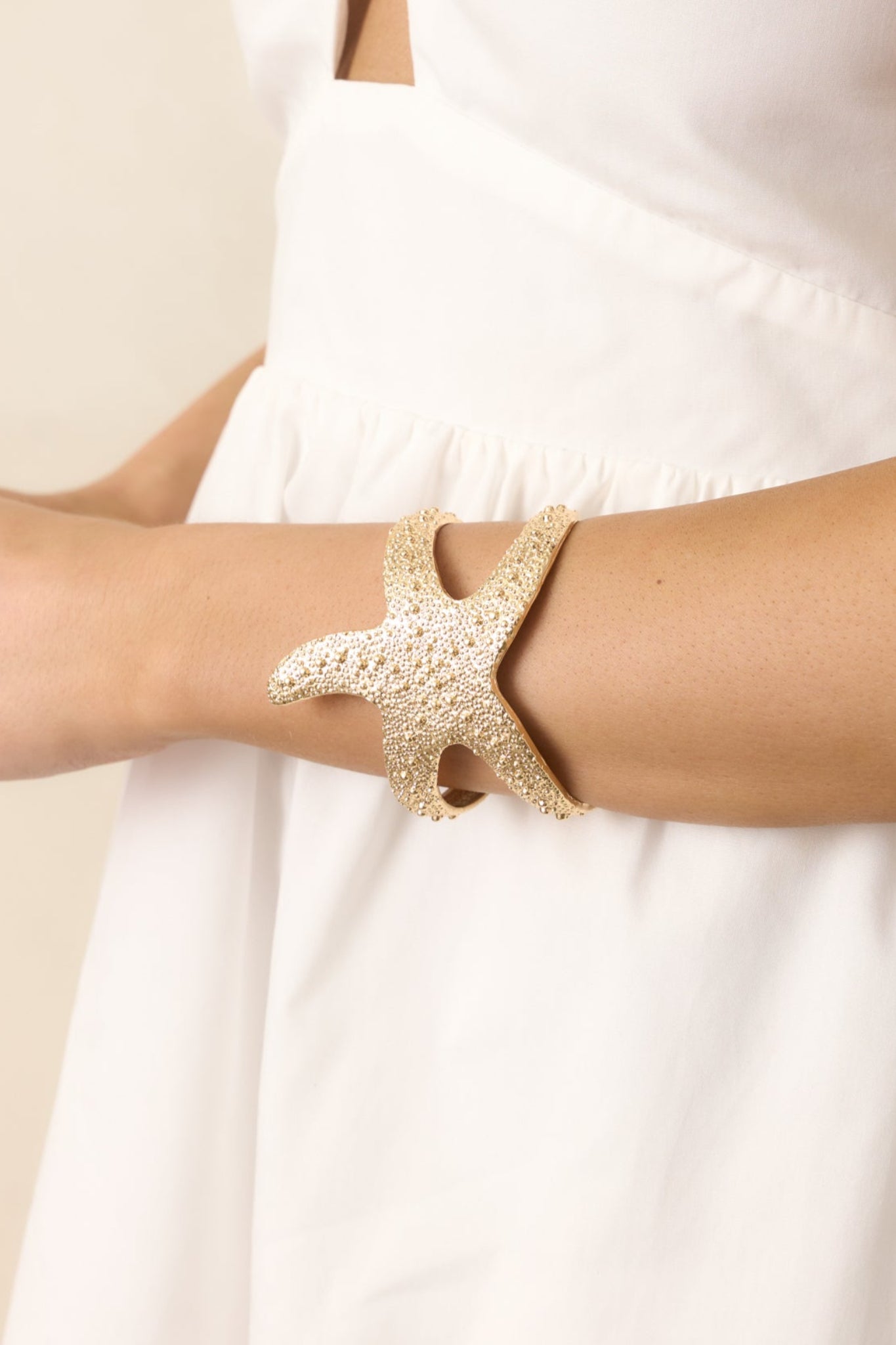A gold starfish bracelet featuring textured gold beads along the top, an adjustable open design, and a charming starfish shape for a coastal-inspired look.