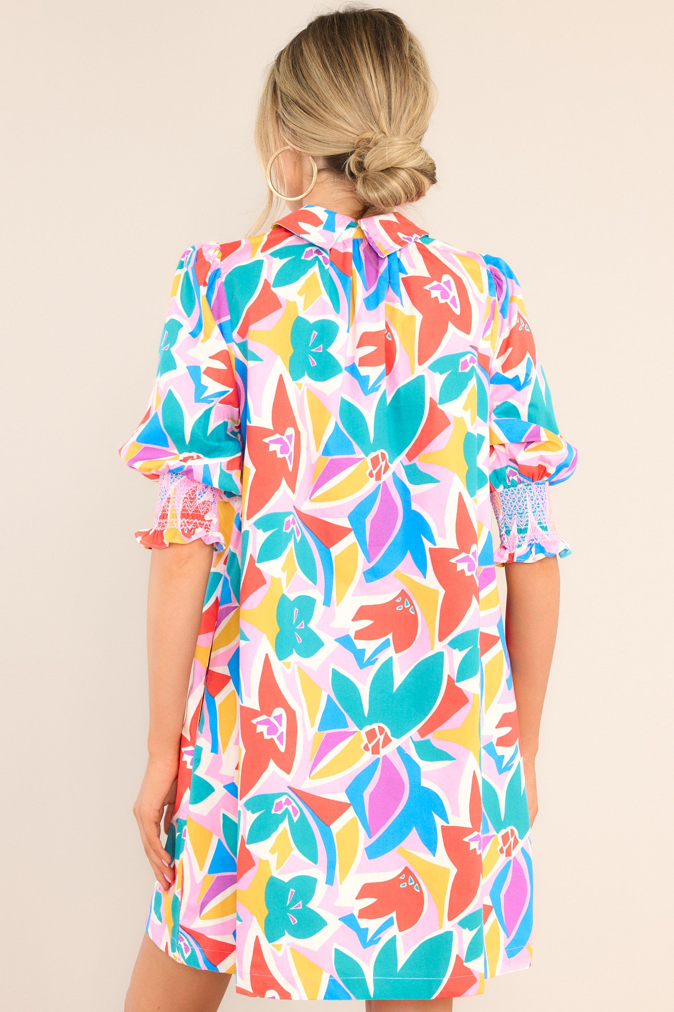 Back view of this dress that features a collared neckline, a smocked chest insert, functional buttons & pockets, and thick elastic cuffed sleeves.