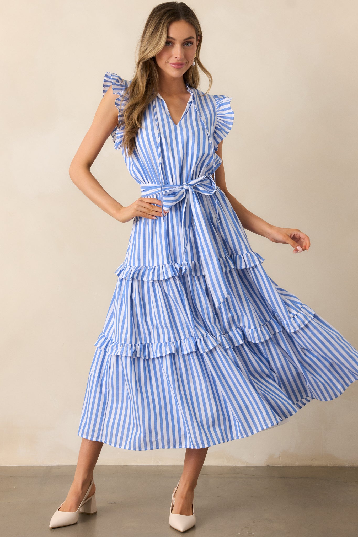 The blue striped fabric, flutter cap sleeves, and tiered ruffle skirt make this dress both breezy and elegant for any occasion.