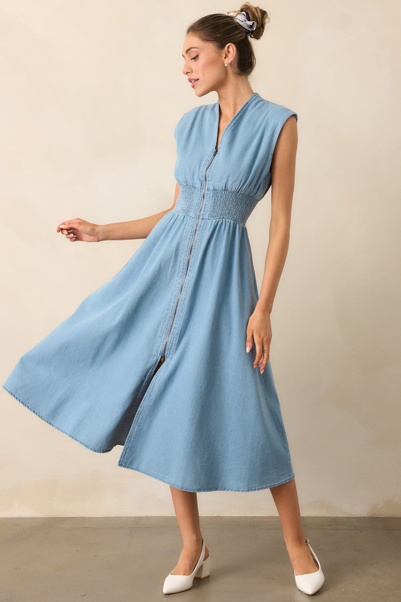 This light wash midi dress features a v-neckline, lightly padded shoulders, and short cap sleeves. The functional full zipper front, smocked waist, and hip pockets add both style and comfort, while the front slit enhances its flowy design.