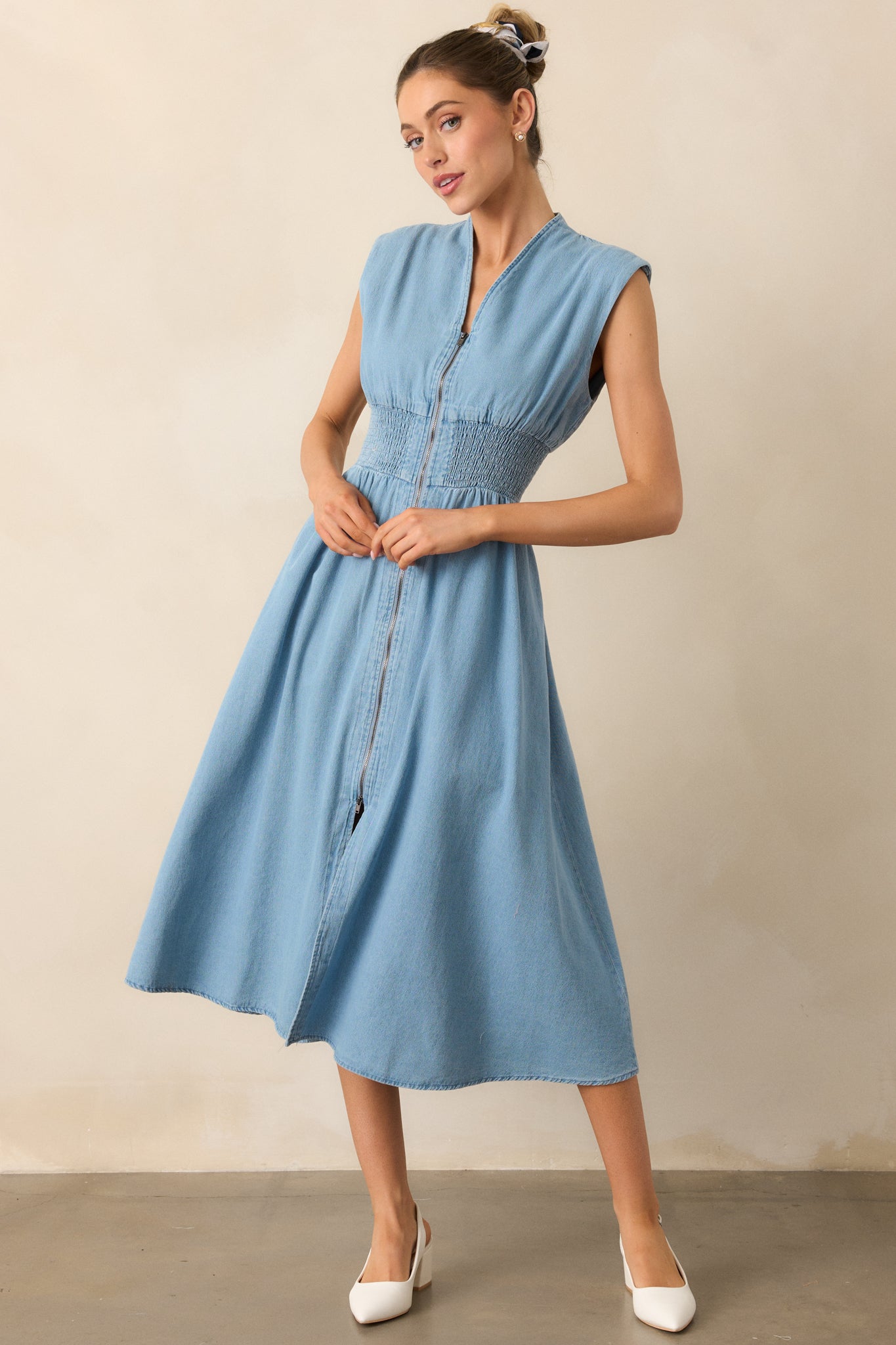 A light wash midi dress with a flattering v-neckline and short cap sleeves, featuring lightly padded shoulders for added support. The smocked waist and functional hip pockets complete the relaxed look, with a chic front slit.