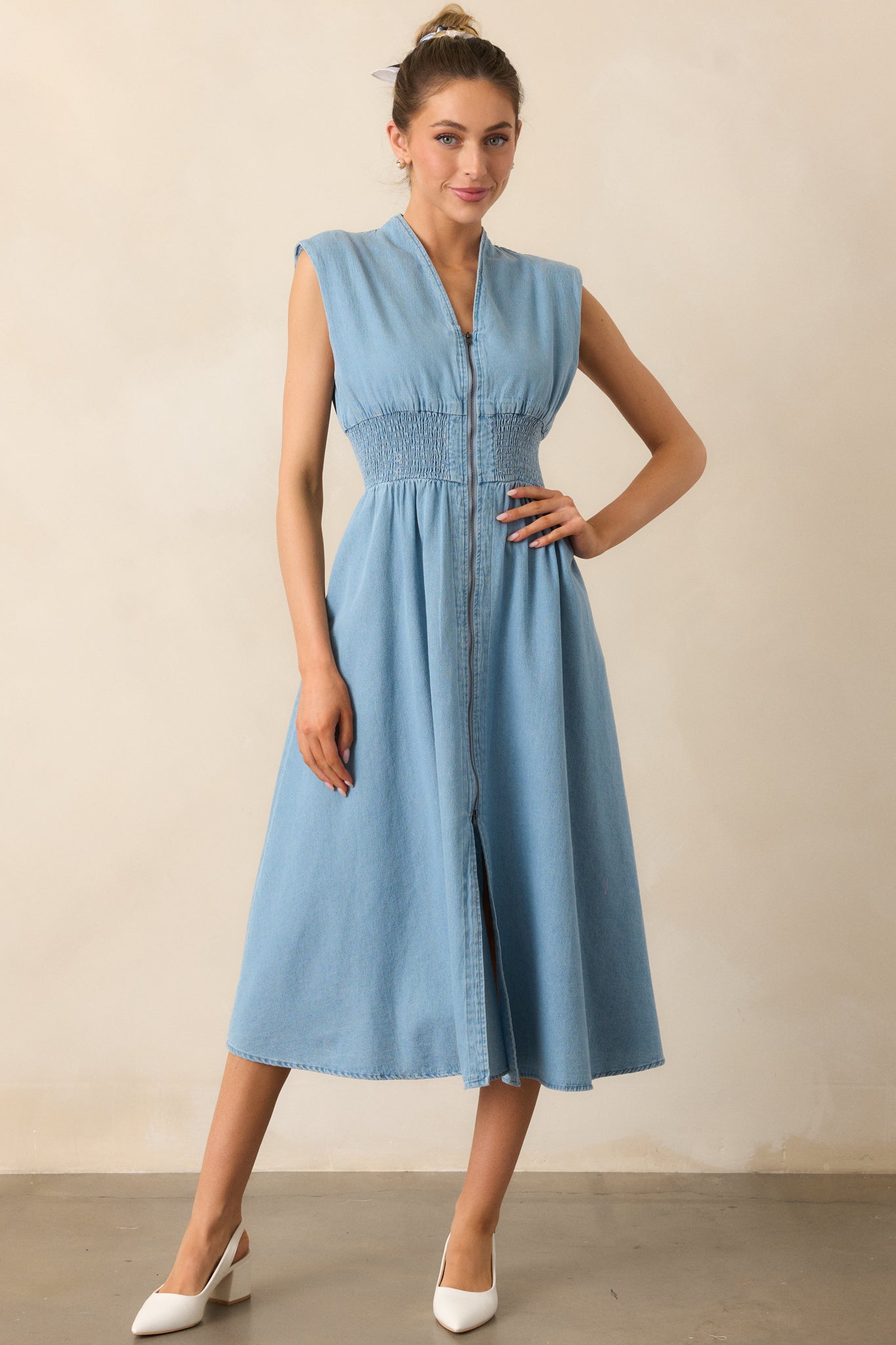 This light wash midi dress showcases a v-neckline, lightly padded shoulders, and short cap sleeves. The functional full zipper front and smocked waist provide comfort and shape, while the front slit adds a touch of sophistication.