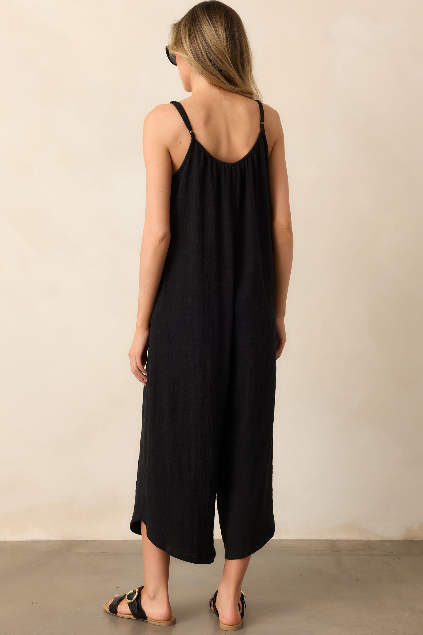 A view from behind of the black jumpsuit showing the scoop back, spaghetti straps, and wide leg flare design.