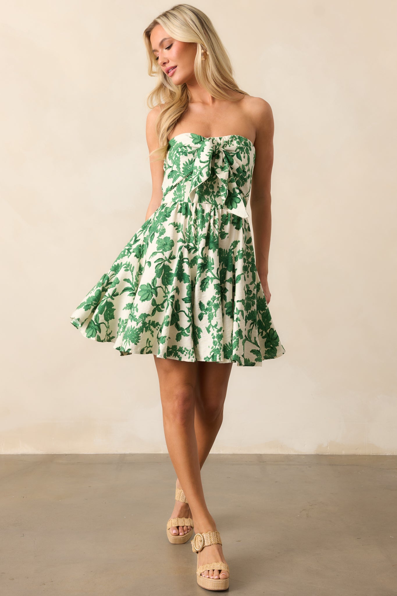 An ivory mini dress with a vibrant green tropical print, featuring a strapless neckline with a self-tie front and a flowy skirt for a relaxed, tropical vibe.