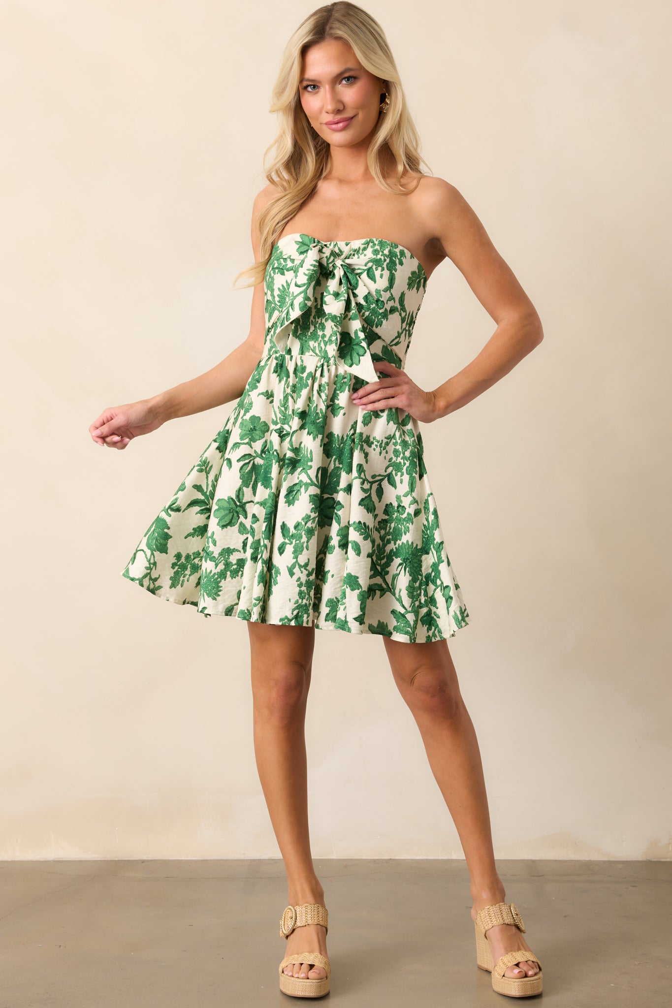 A playful ivory mini dress with a tropical green print, a strapless neckline with a self-tie front, and a flirty flowy skirt for a carefree style