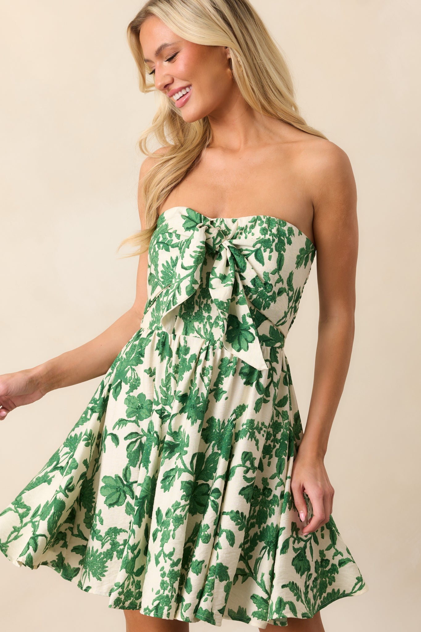 A closer look at the self-tie front detail and tropical print, highlighting the strapless neckline and feminine design of the ivory mini dress.