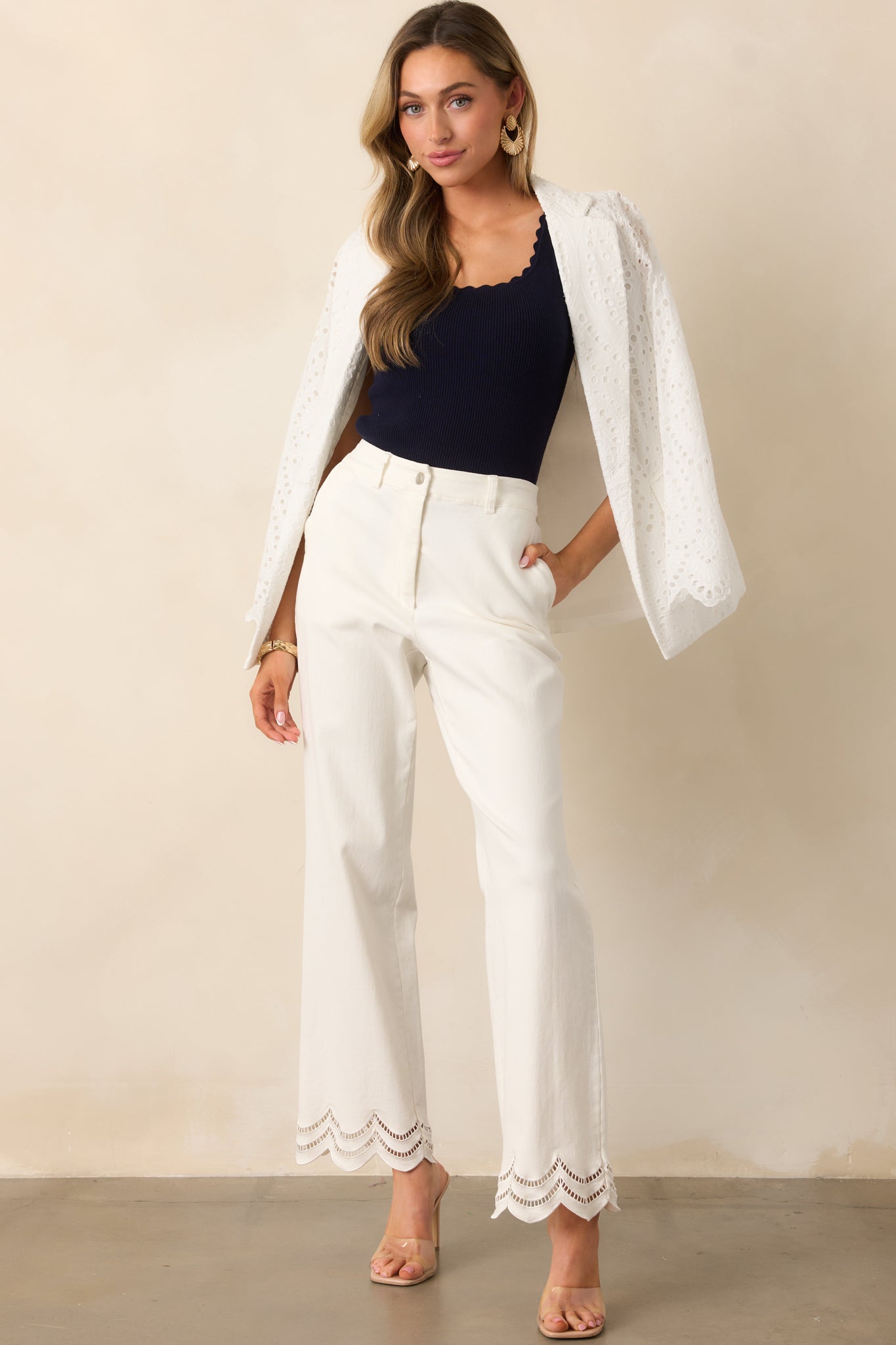 A full view of the white jeans featuring a high-waisted design, back elastic waist insert for comfort, and scalloped bottom hems with open embroidered eyelet details for a chic touch.