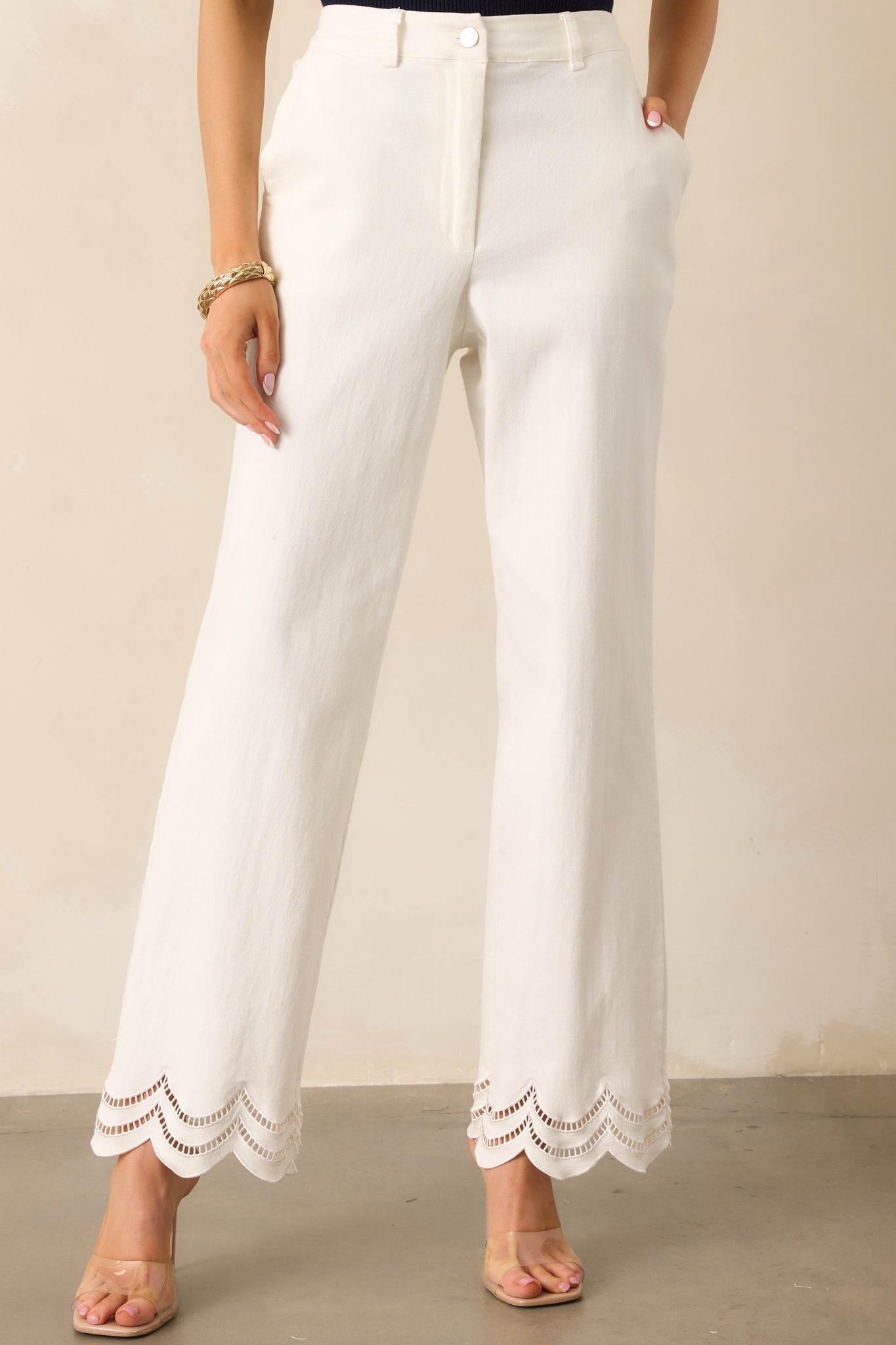 A close-up of the waistband and back elastic waist insert, showcasing the button and zipper closure, belt loops, and the scalloped embroidered eyelet details along the bottom hems.