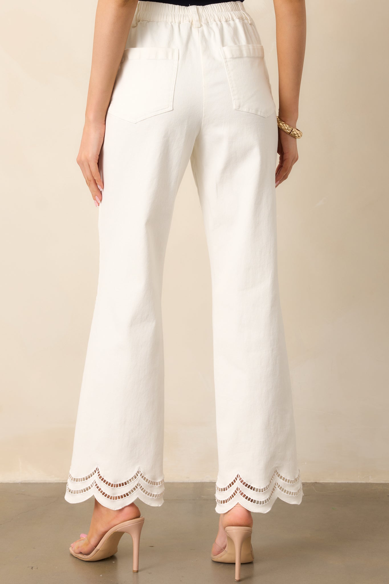 The back view of the white jeans, showing the back elastic waist insert and functional pockets, with the scalloped embroidered eyelet details adding a refined touch.