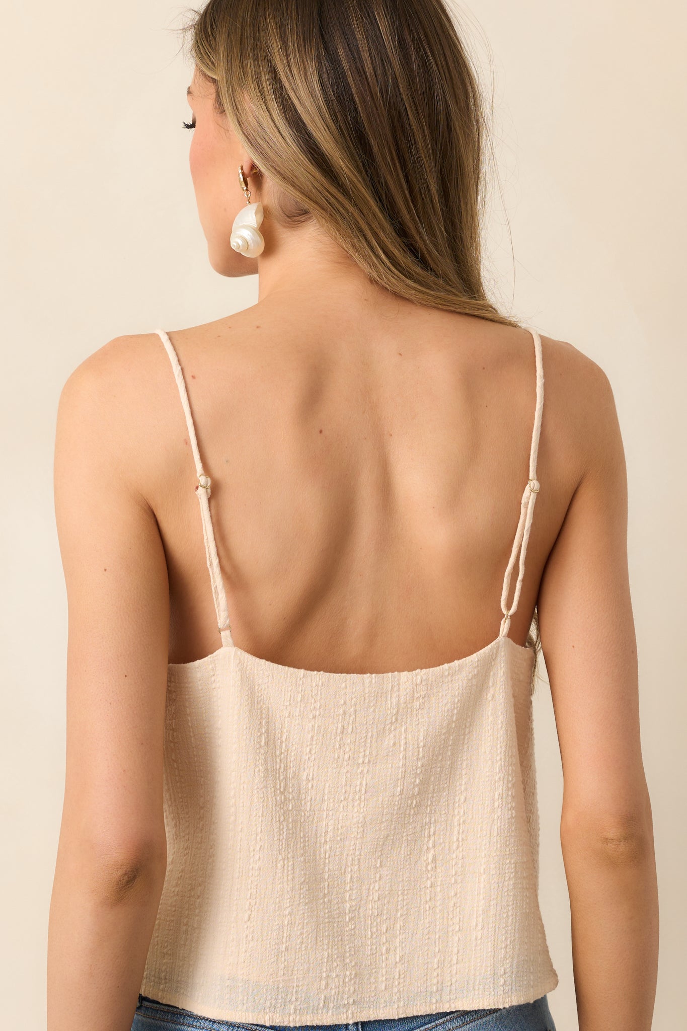 A view from behind of the beige tank showing the adjustable straps and relaxed cropped fit across the upper back.