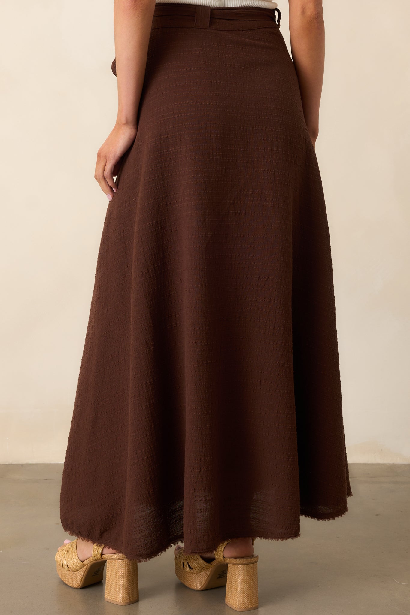 A view from behind of the brown skirt showing the high-waisted cut and clean lines with a frayed hem.