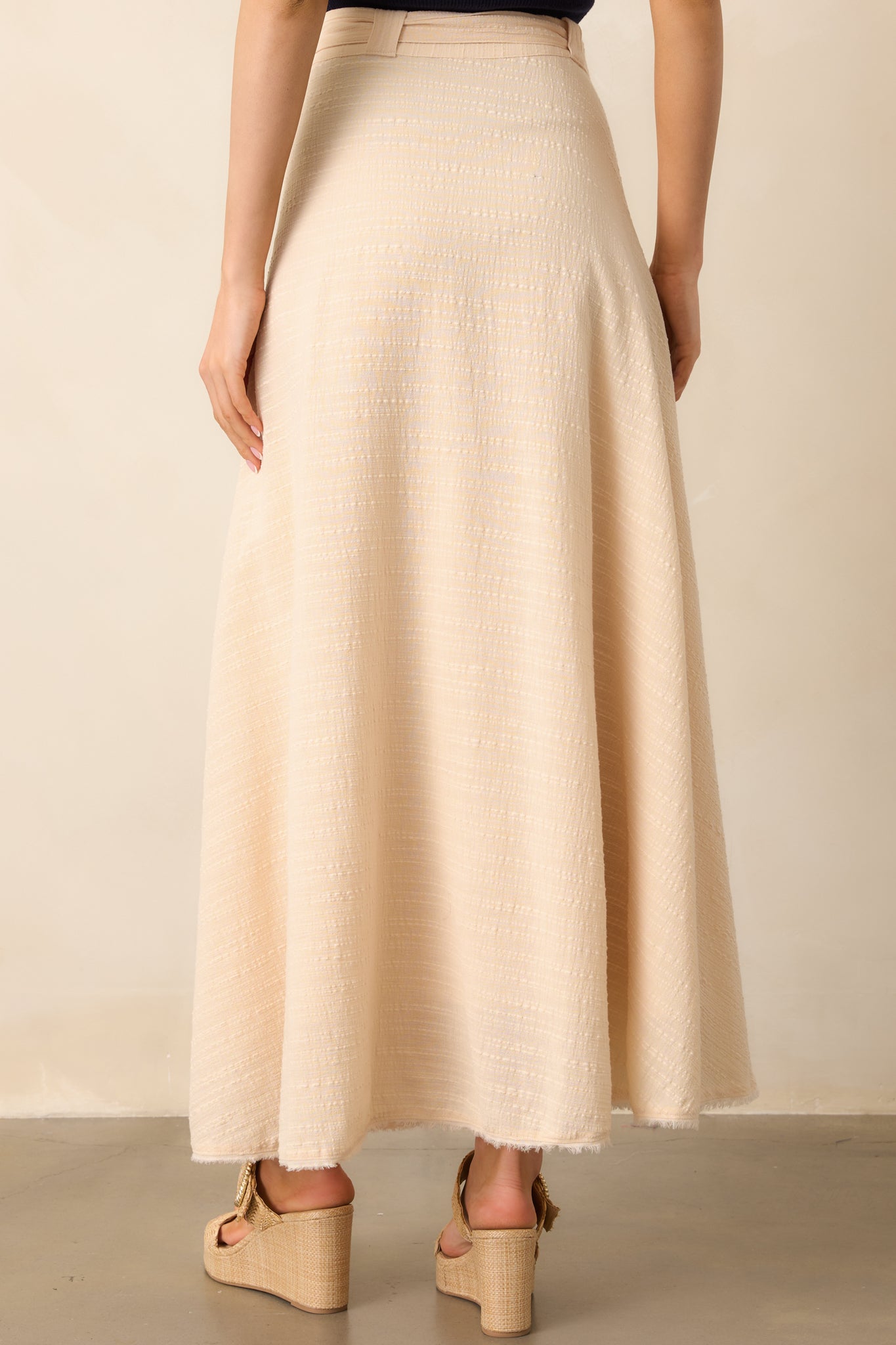 A view from behind of the beige skirt, showing the clean lines and high-waisted cut with the raw frayed hem.
