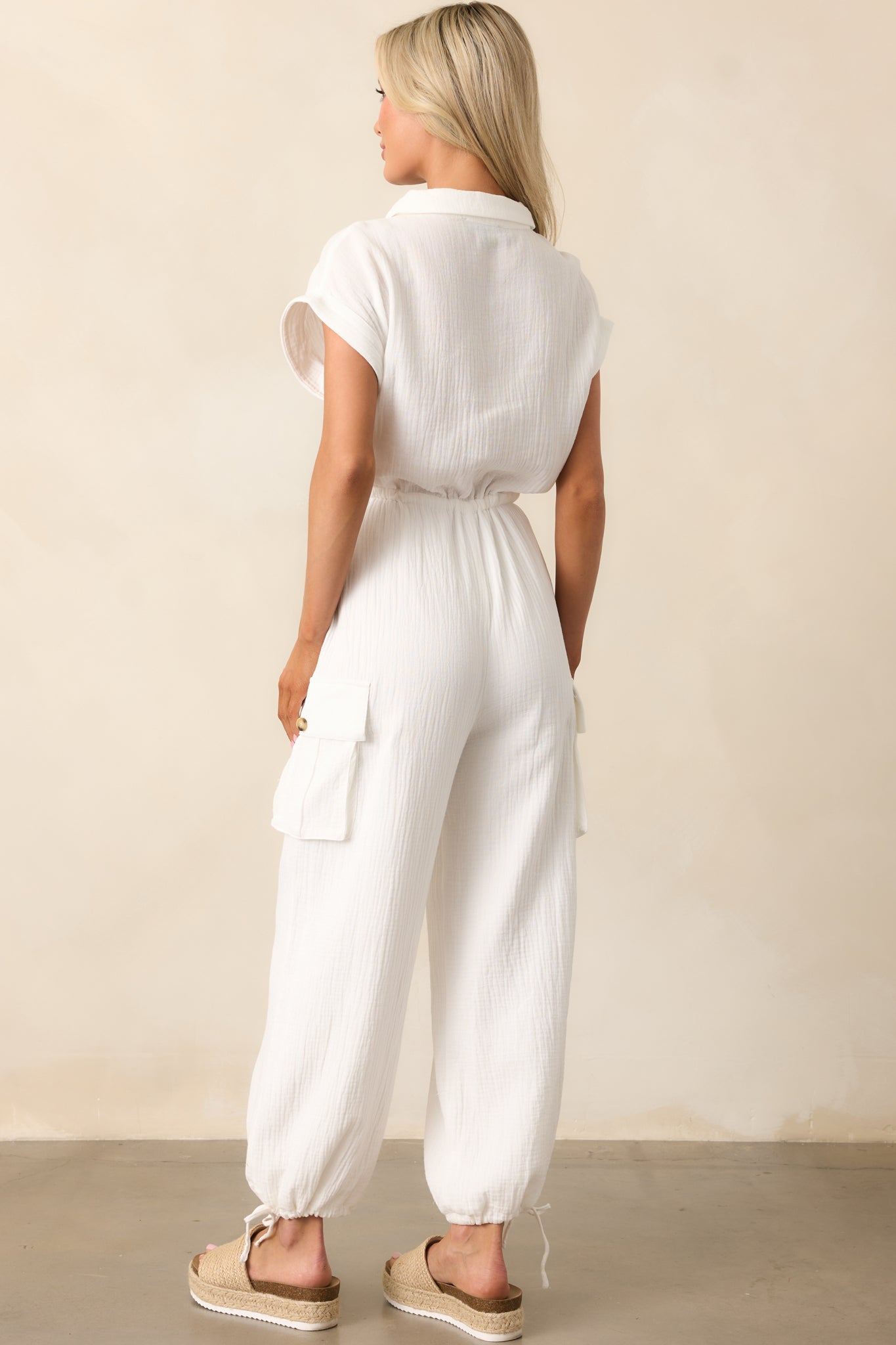 The back of the jumpsuit featuring a plain design with seam detailing, folded short sleeves, and a tied waist.