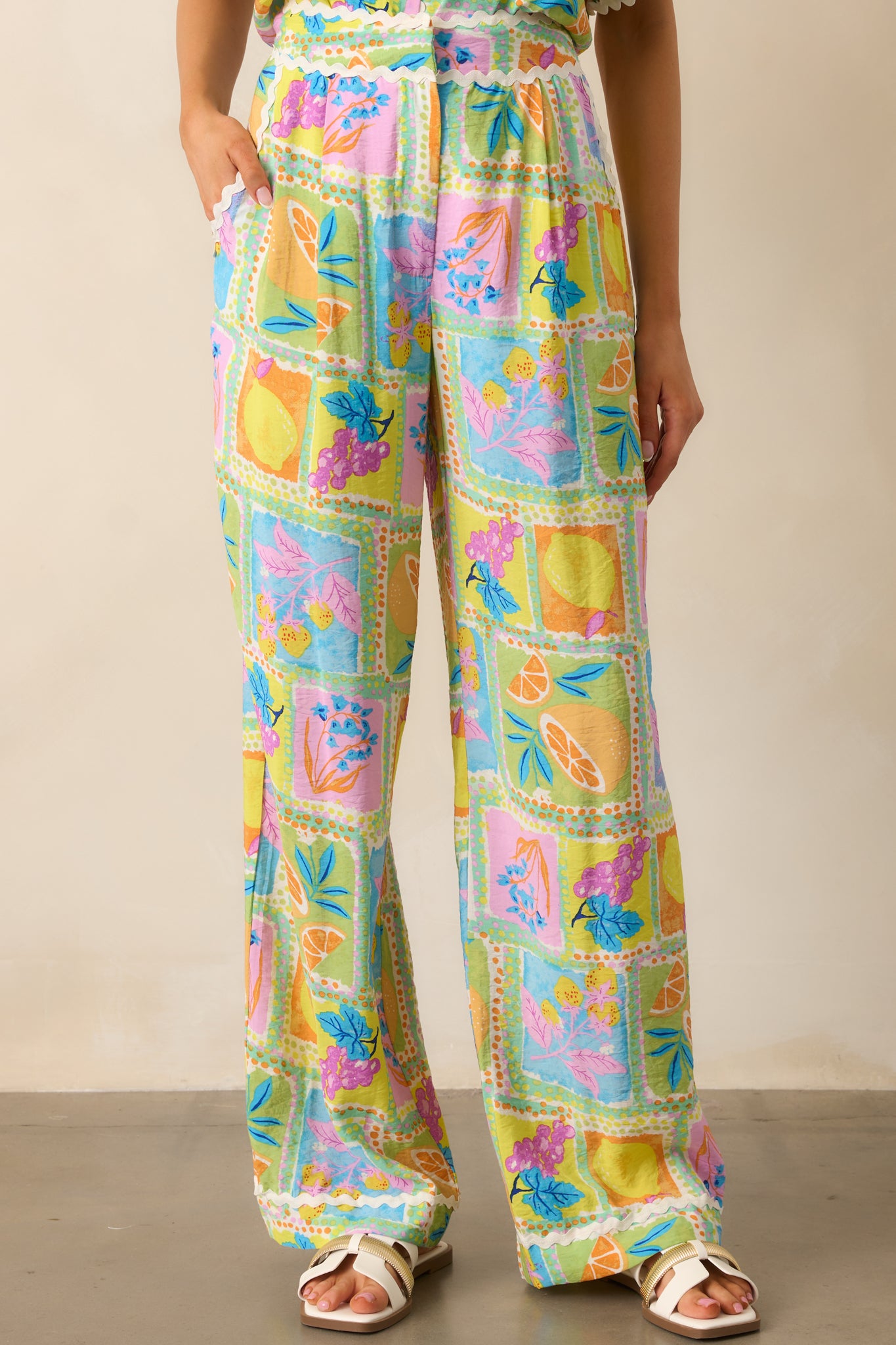 Front view of green pants featuring a high waisted design, hook & bar closure, zipper, functional hip pockets, a unique print, a wide leg design, and ricrac trim.